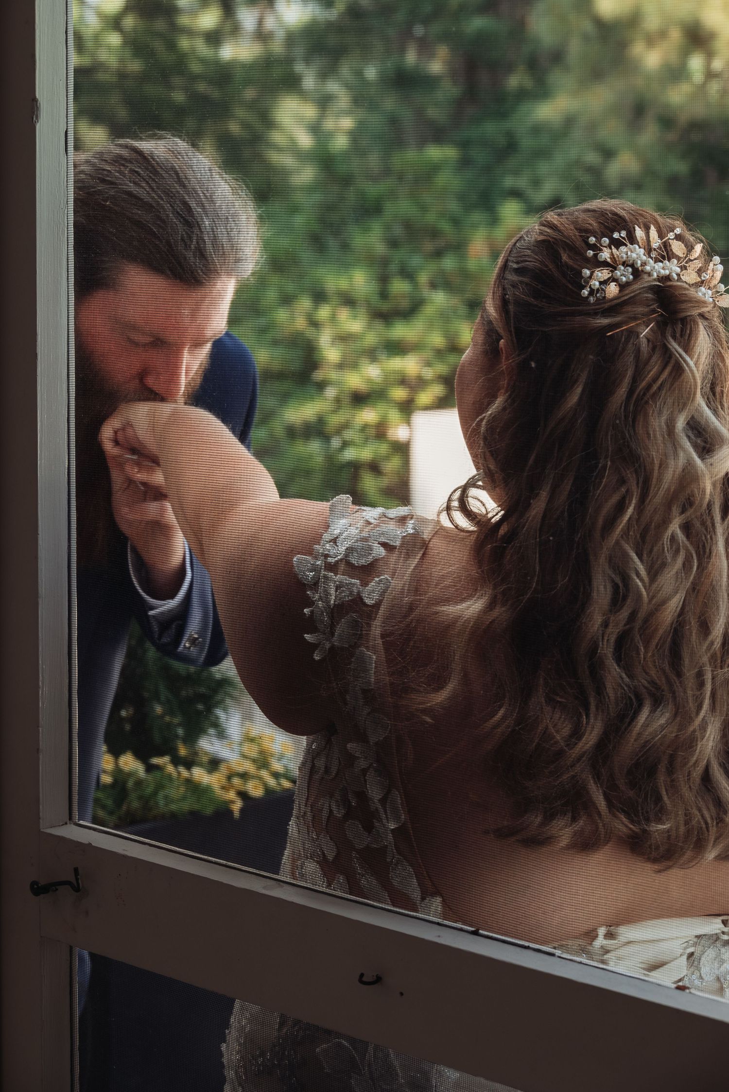 Groom kisses bride's hand through doorway in romantic wedding day first look moment.