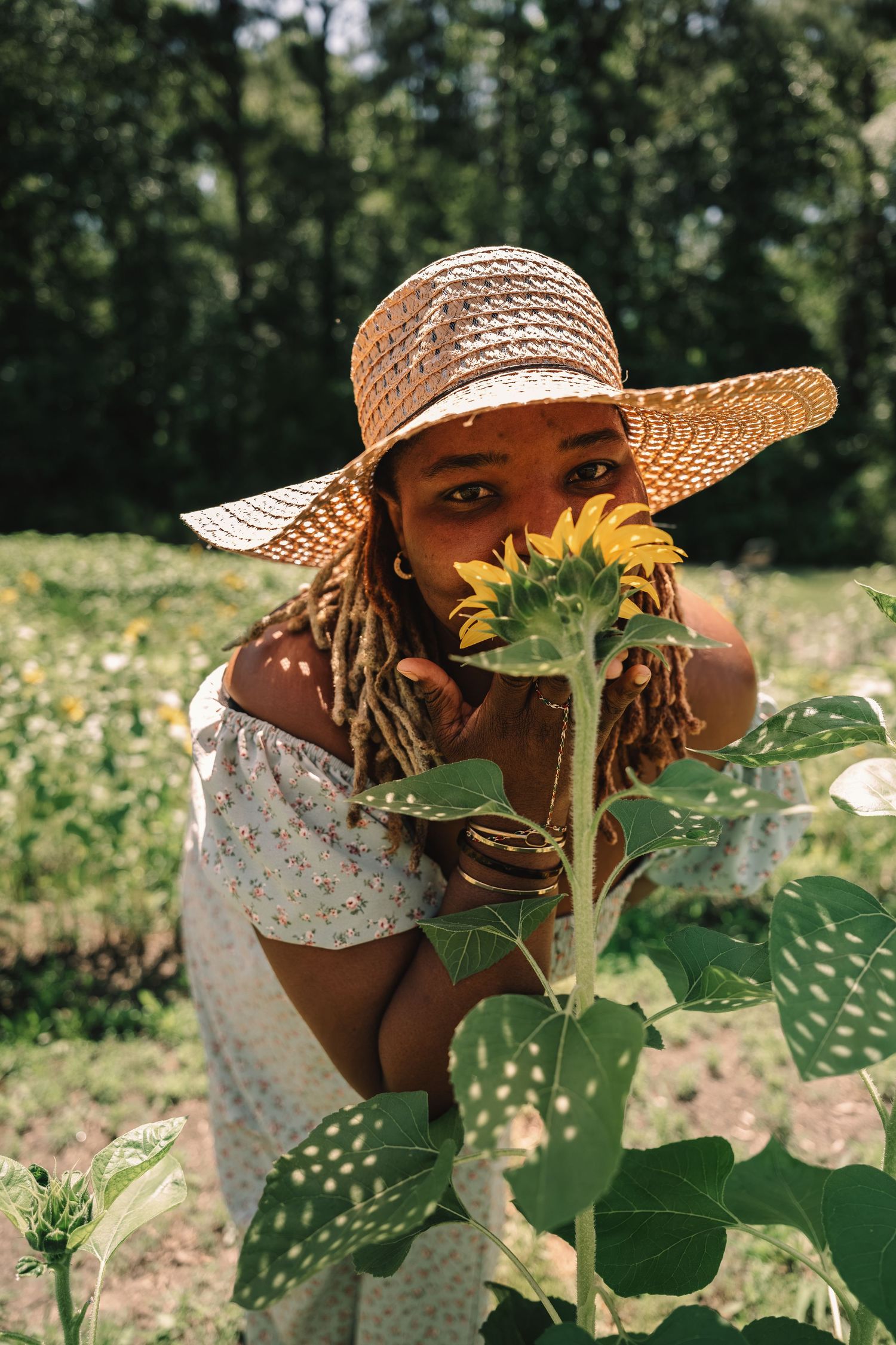Young woman in a straw hat smelling a bright yellow sunflower in a sunny outdoor garden field.
