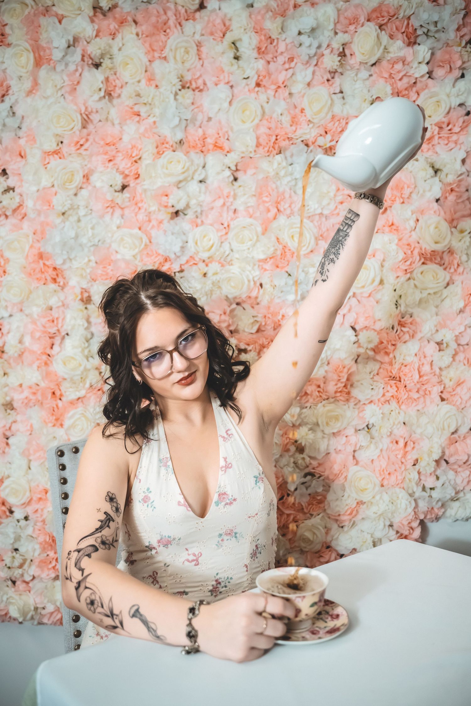 Person in glasses poses against floral backdrop in white sleeveless top showing various expressions and poses.