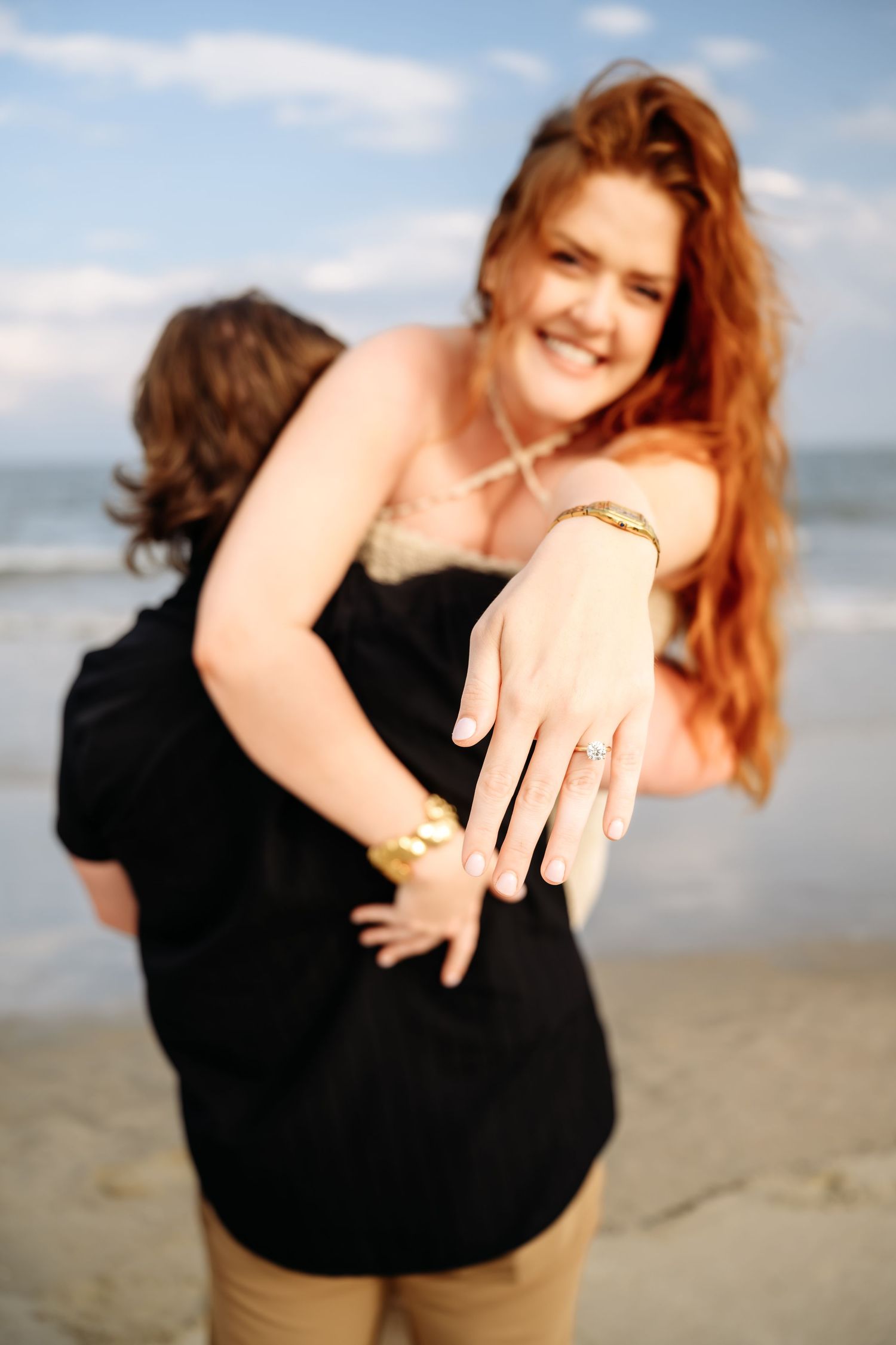 Smiling redhead woman showing off her engagement ring on a beach after proposal.