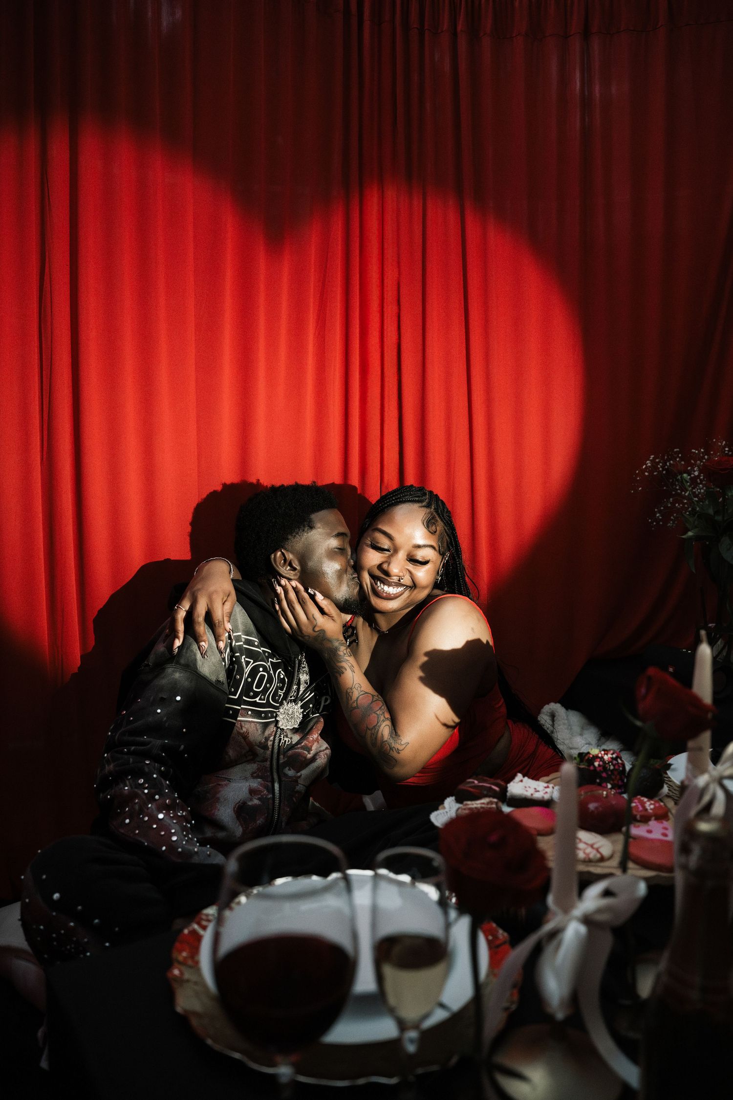 Couple shares joyful moment under heart-shaped spotlight against red curtain backdrop at romantic event.