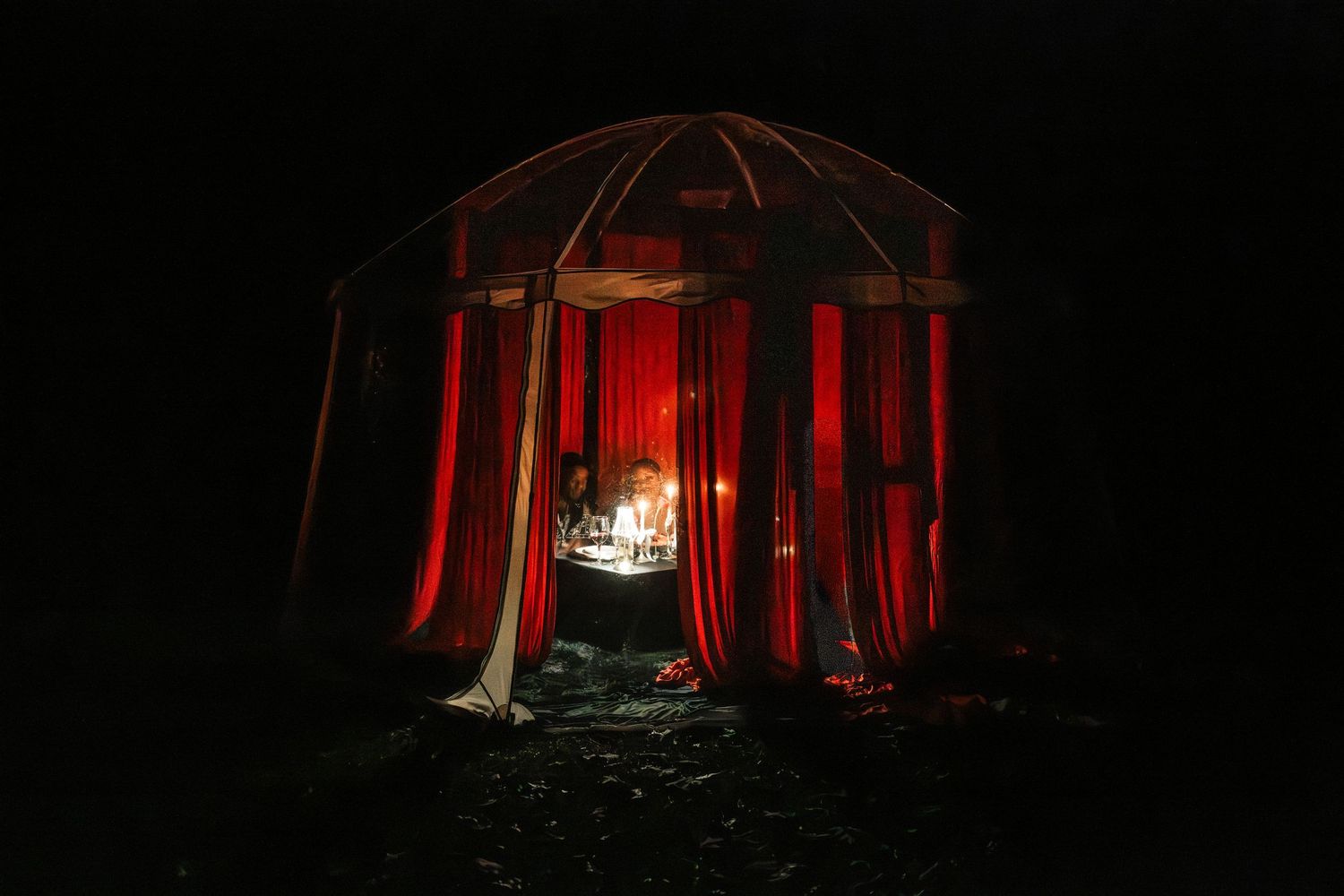 Intimate candlelit gazebo with red curtains glows warmly against dark night sky at romantic event.