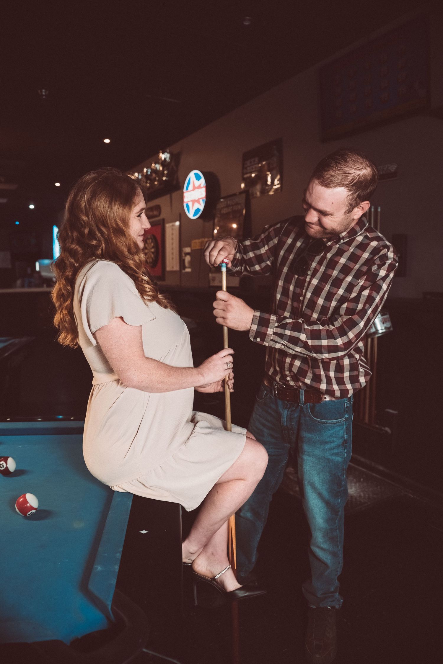 A couple dancing and twirling on a dance floor next to blue pool tables in a dark venue.