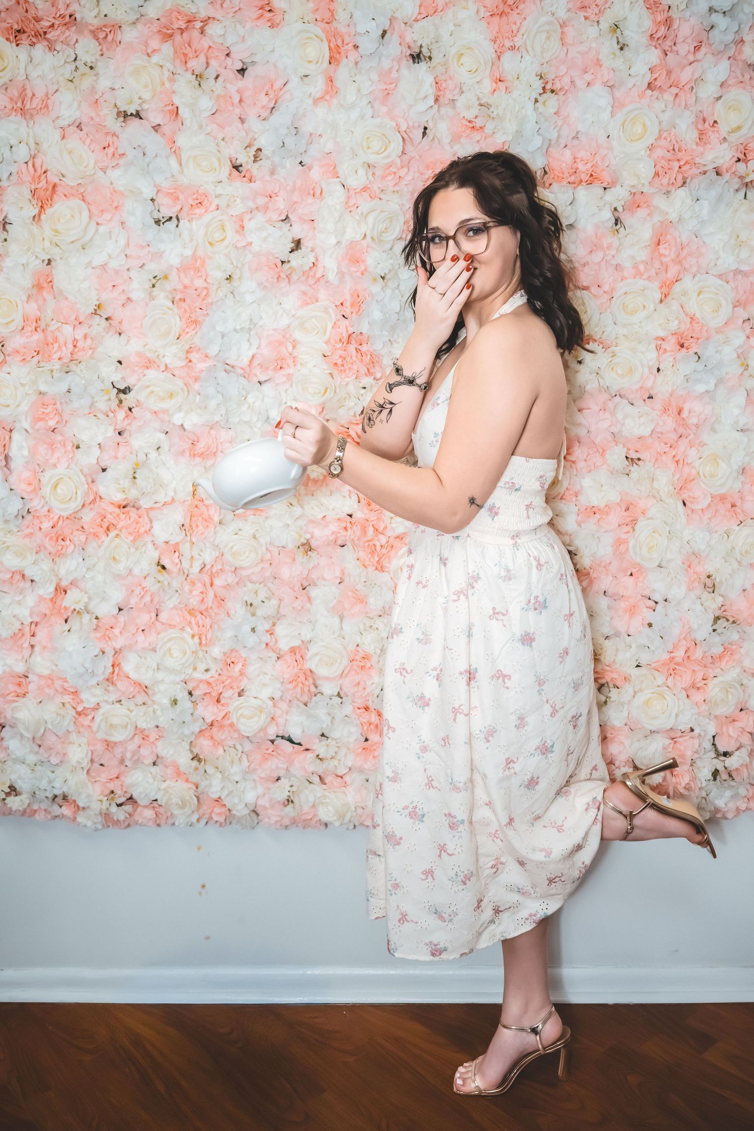 A series of photos against a floral wall backdrop showing poses in a white dress and glasses on wooden flooring.