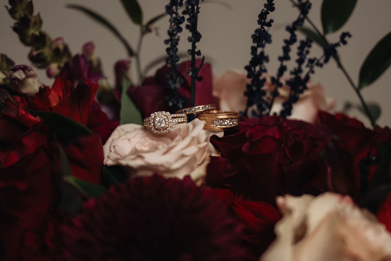 Gold wedding rings resting on deep red and blush wedding bouquet with lavender accents.