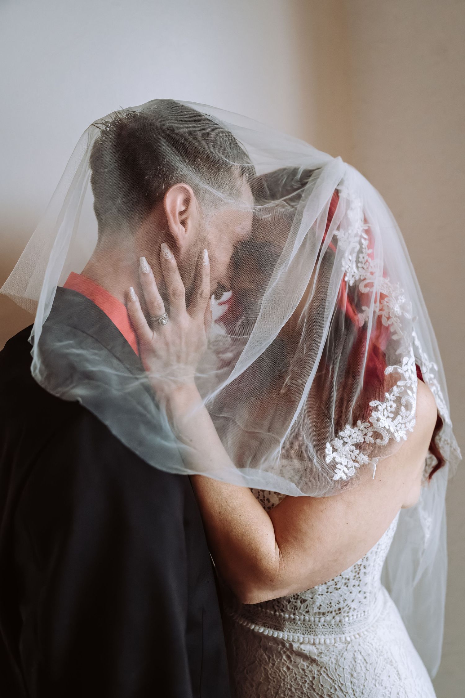 Bride and groom sharing an intimate kiss hidden under a white lace wedding veil.