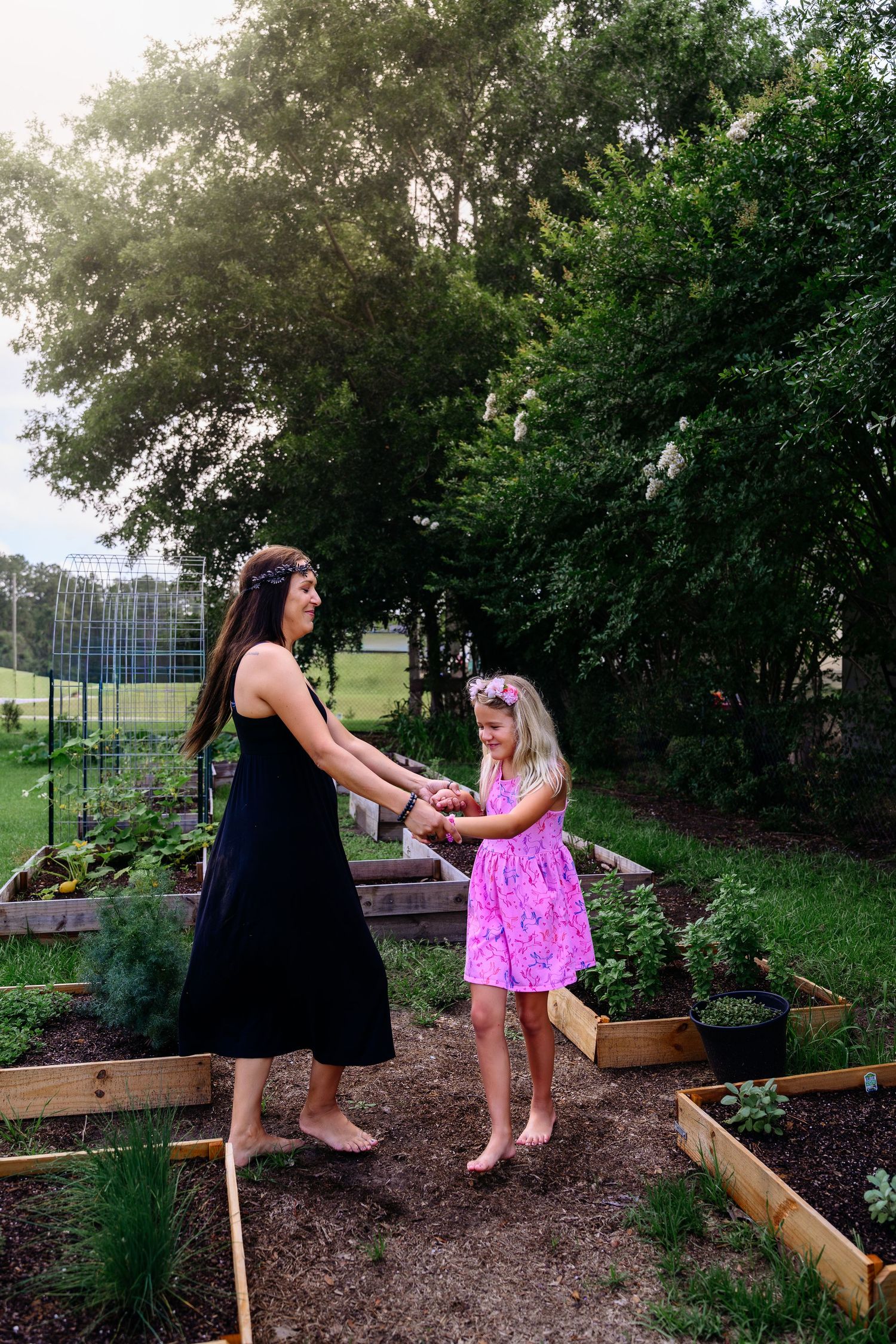 Woman in black dress and girl in pink dress holding hands in a lush garden.