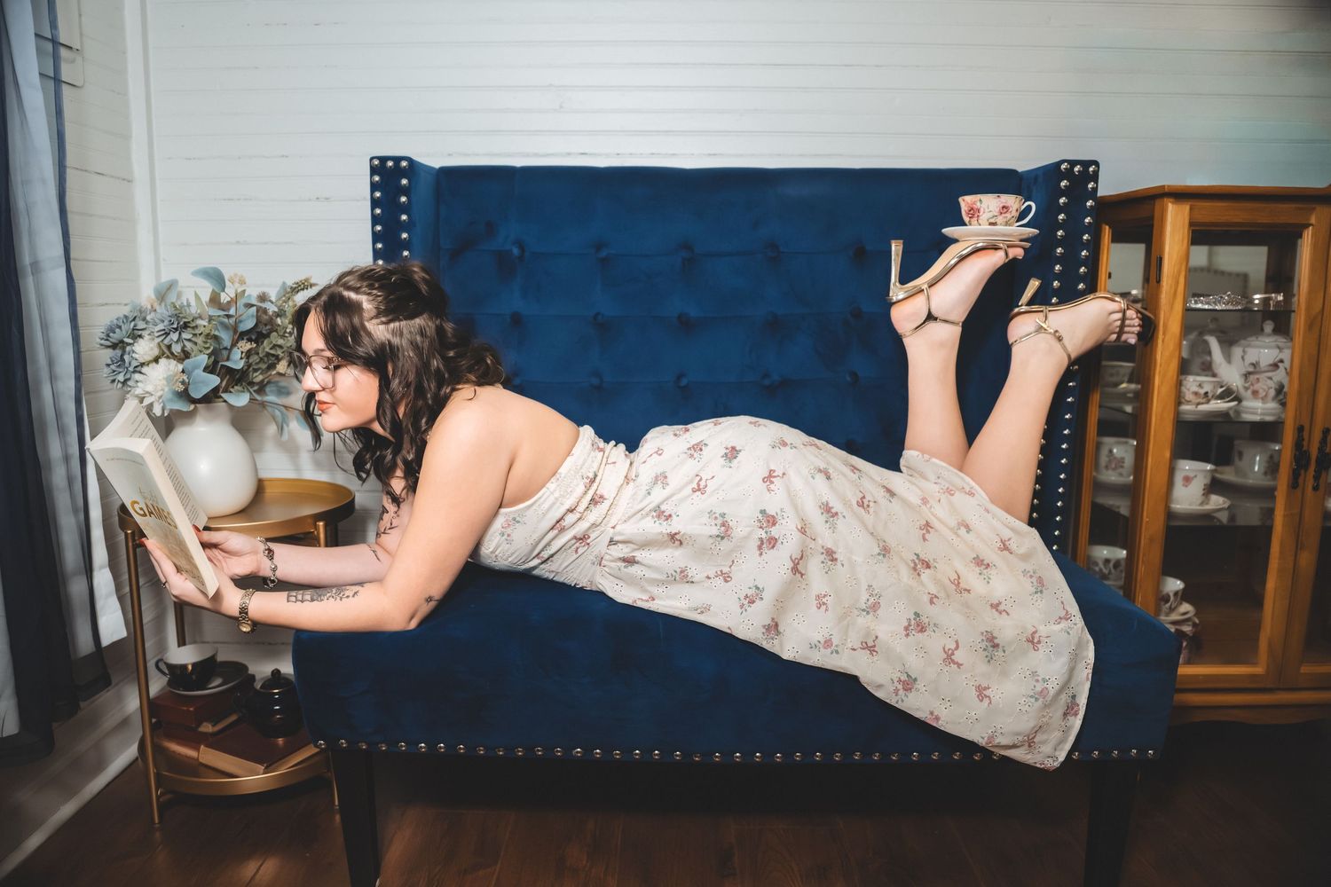 Person in a floral dress lying on a blue couch in a series of different poses.