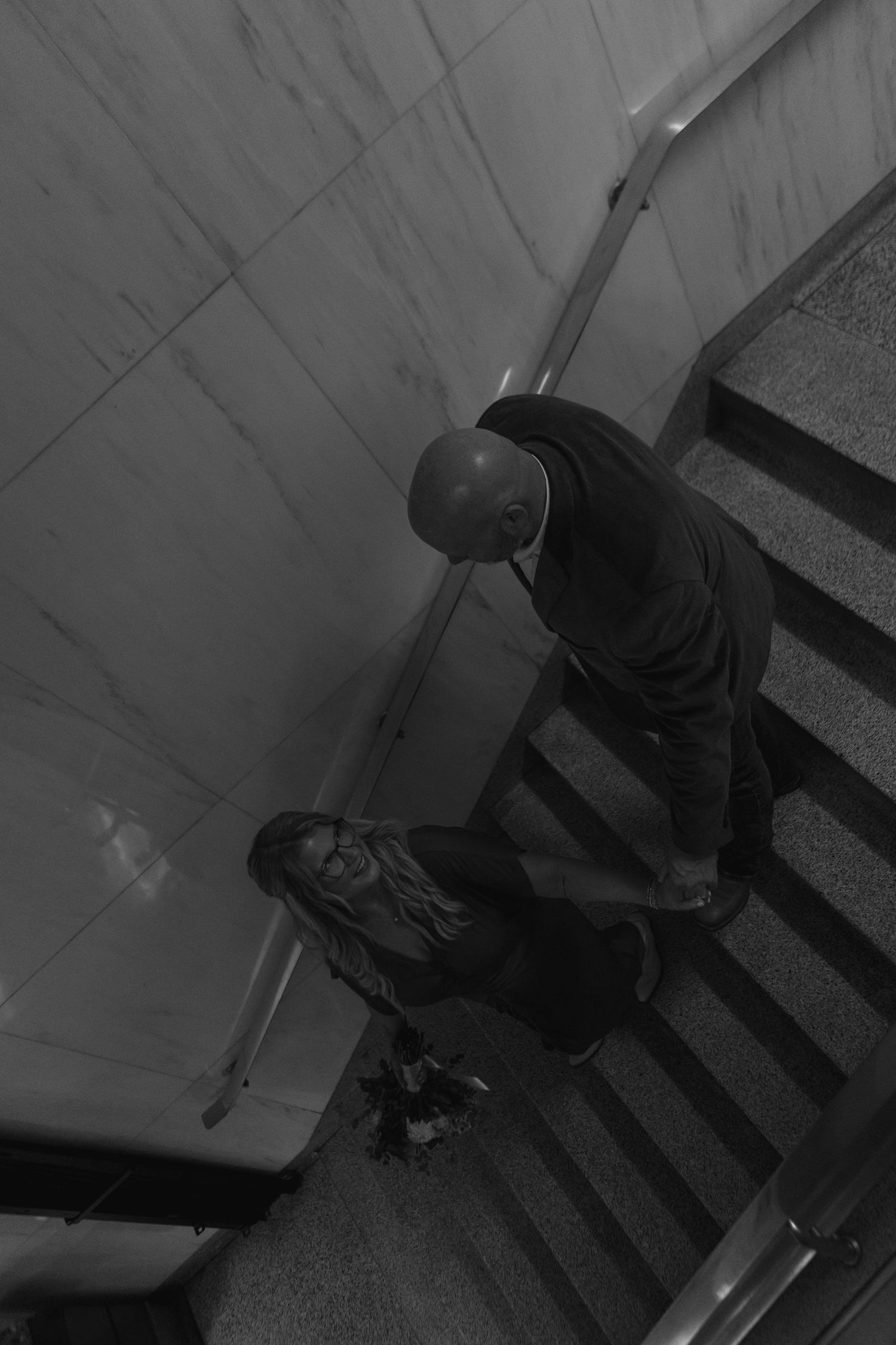 Black and white overhead shot of couple sitting together on marble staircase steps.