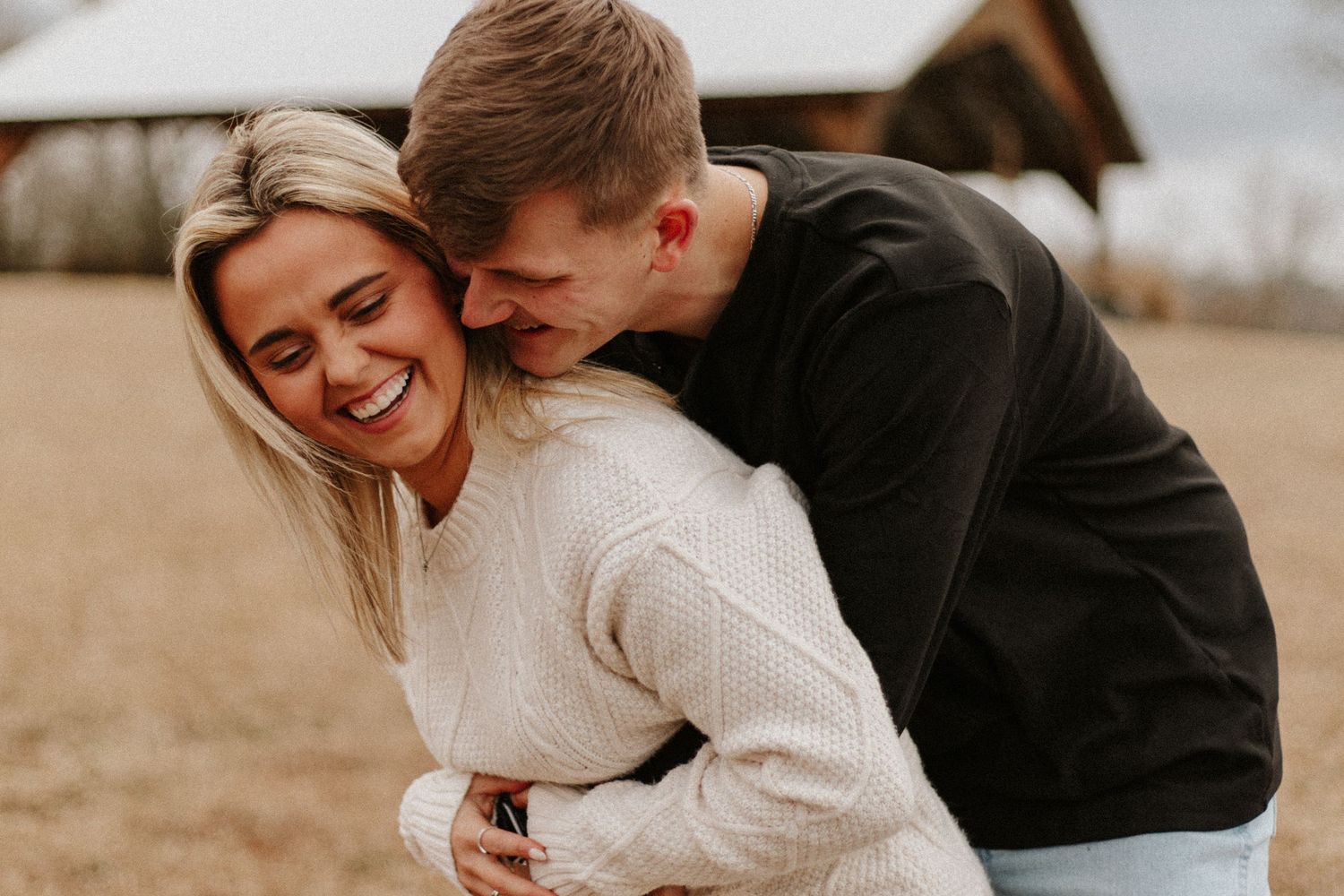 Man hugging woman from behind as she laughs joyfully outdoors in a snowy winter setting.