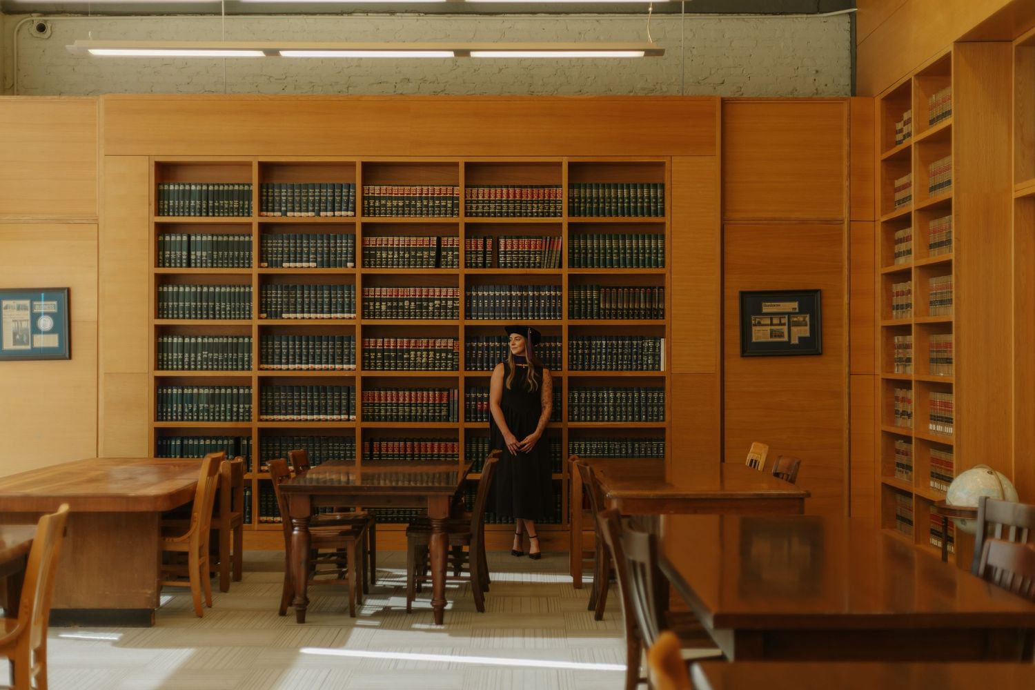 Woman standing alone in wood-paneled law library surrounded by floor-to-ceiling bookshelves.