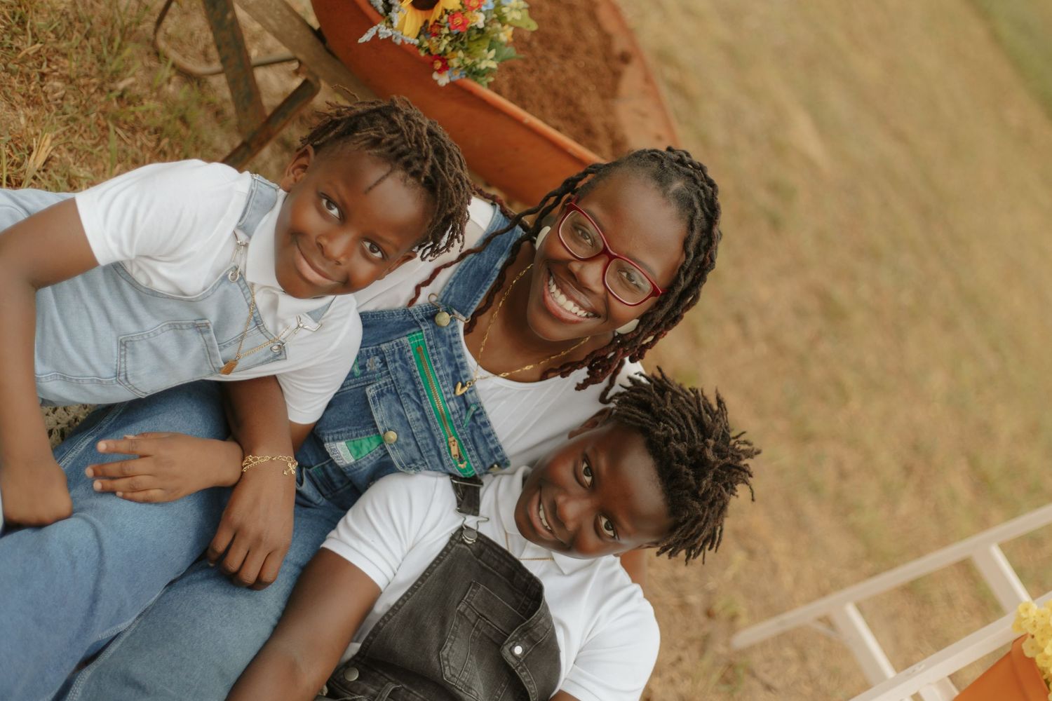 Three smiling people pose together outdoors in casual denim and white outfits on sunny day.