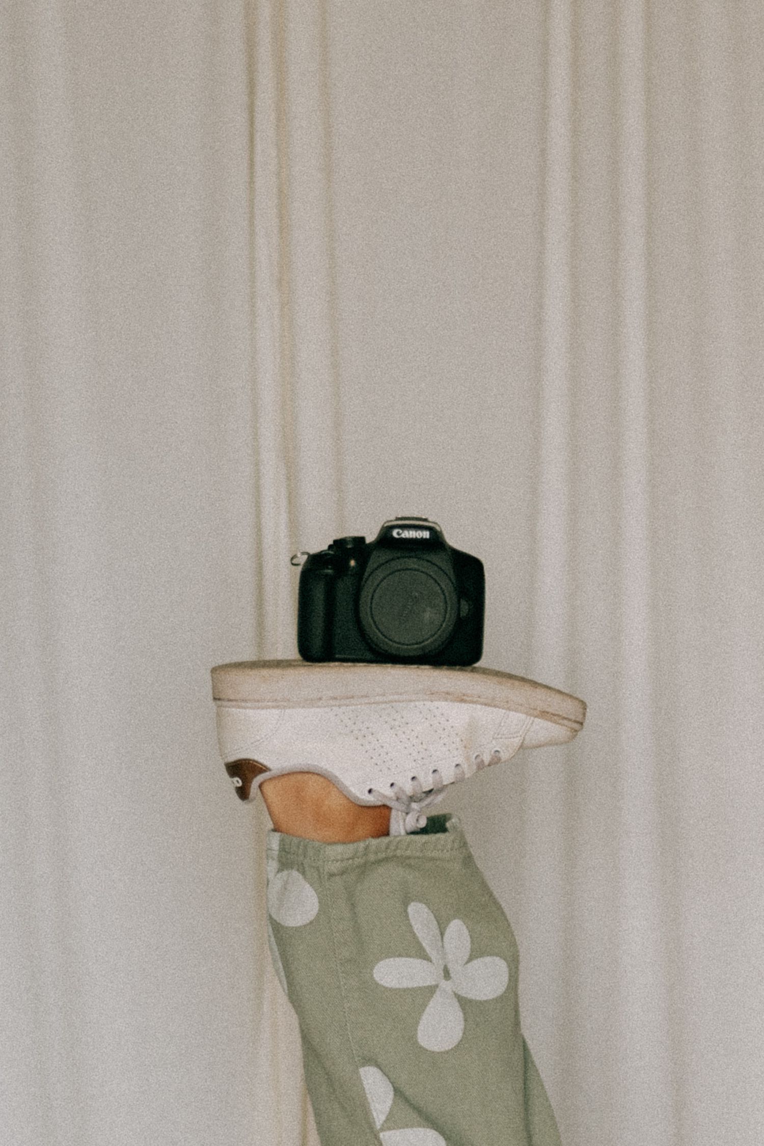 Canon DSLR camera balanced on a foot wearing white sneaker and floral pants.