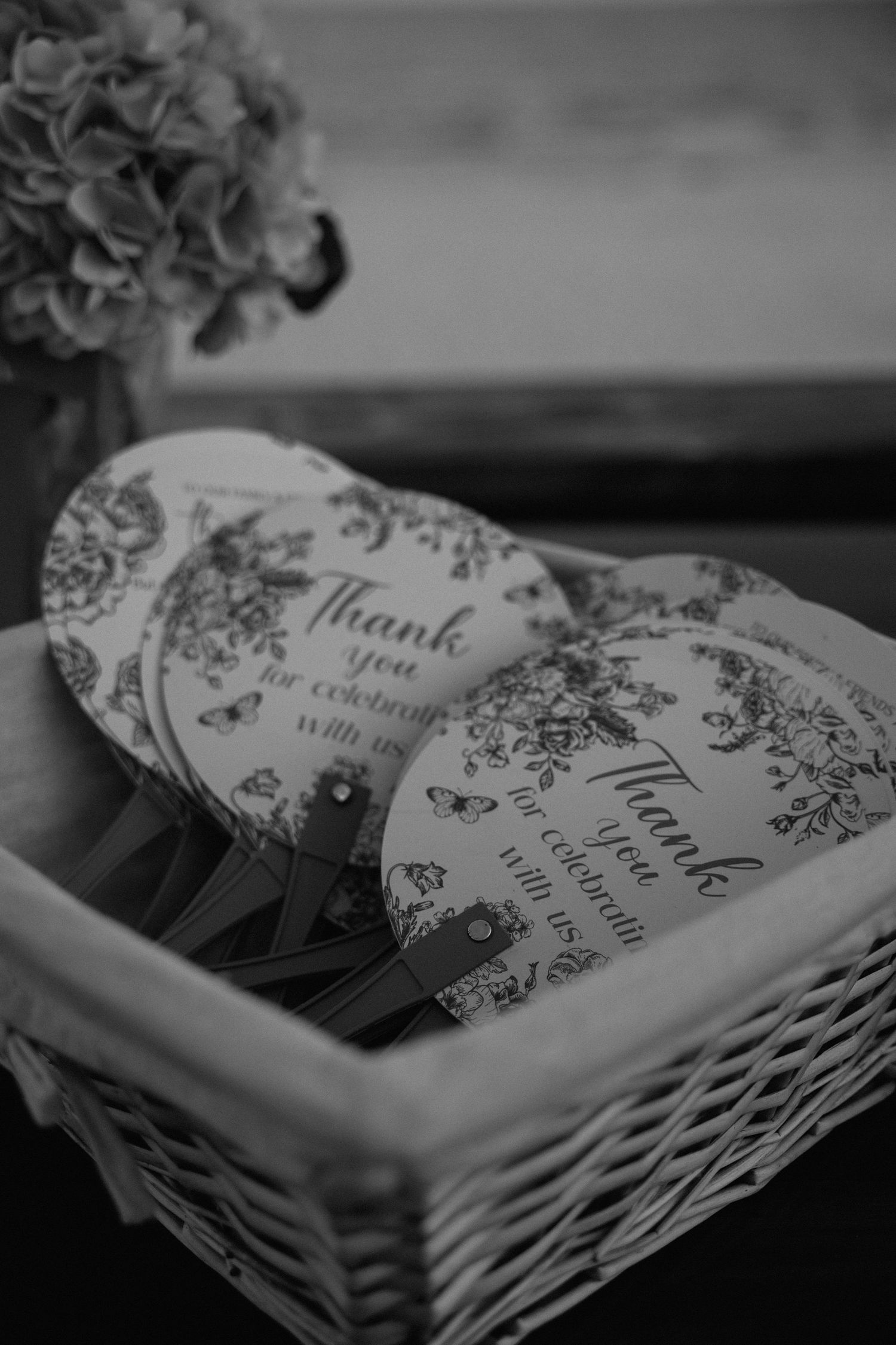 Heart-shaped wedding favor fans with floral design in wicker basket reading Thank You for celebrating with us.