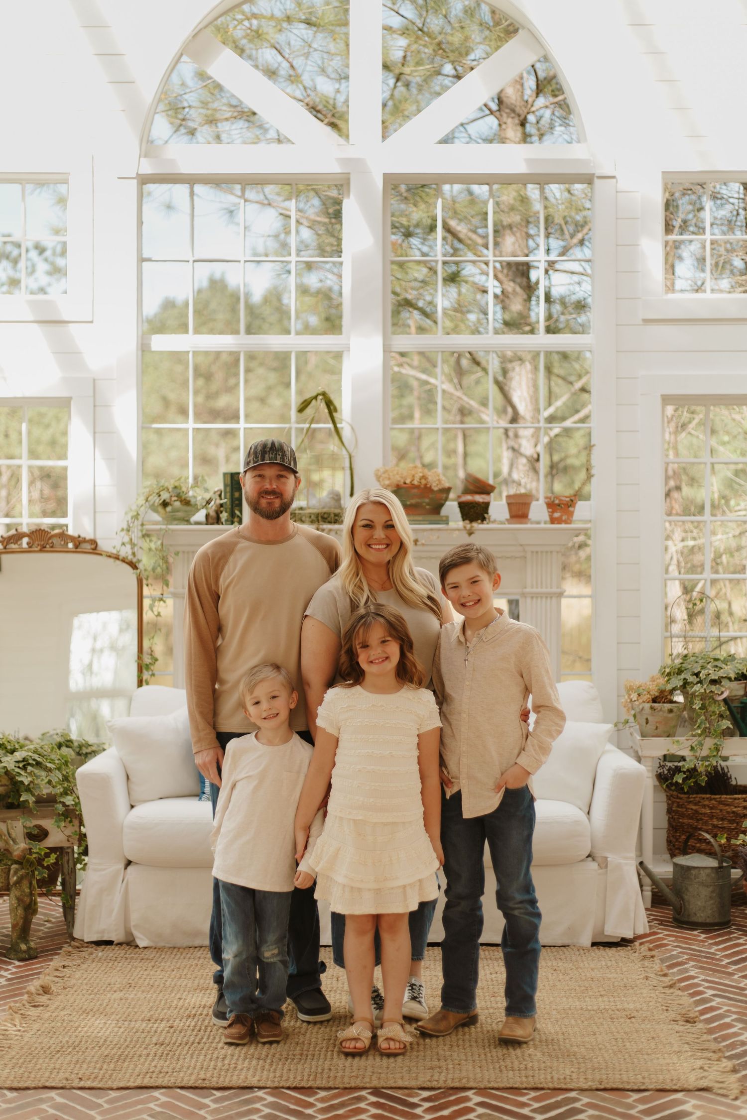 Family of five posing in a sunlit room with arched windows and white decor.