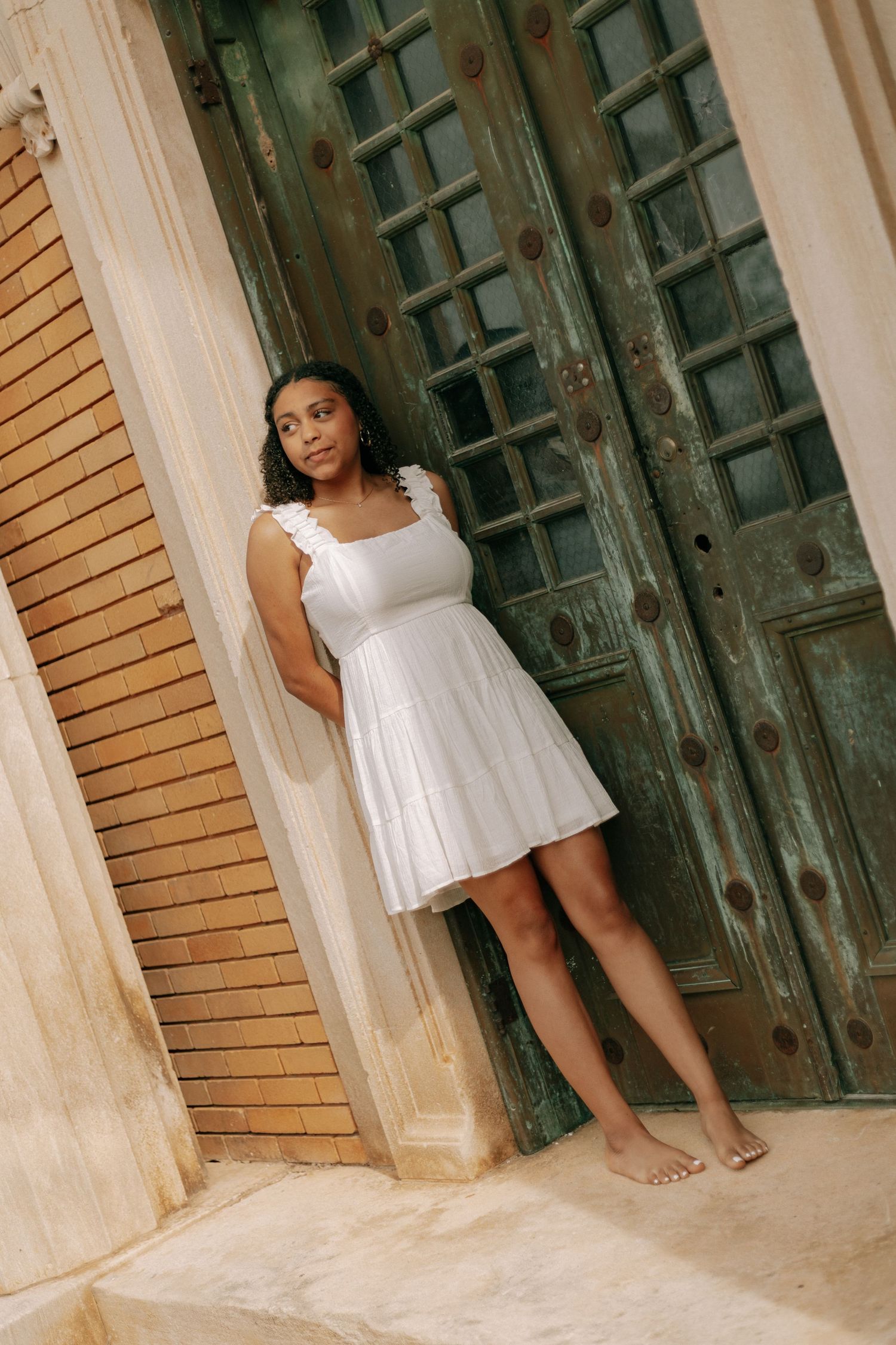 Young woman in white dress leaning against ornate vintage wooden doors.