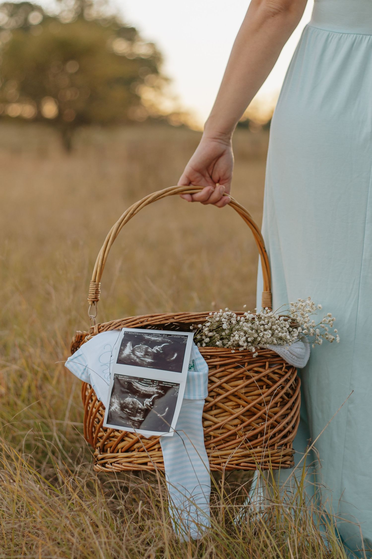 Woman in mint dress holding wicker basket with ultrasound photos and baby's breath flowers.