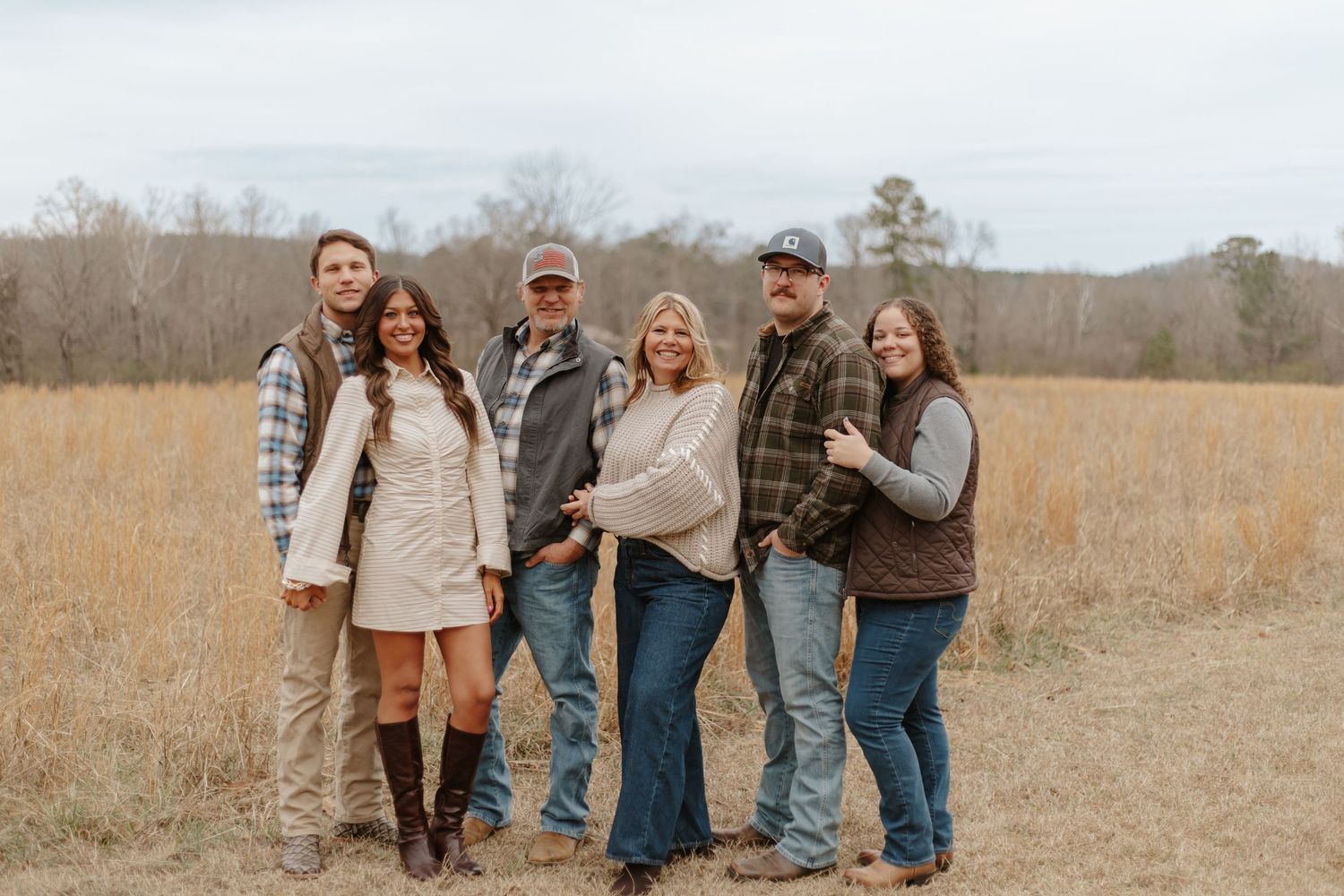 Six family members pose together smiling in an open field during a cool autumn day.