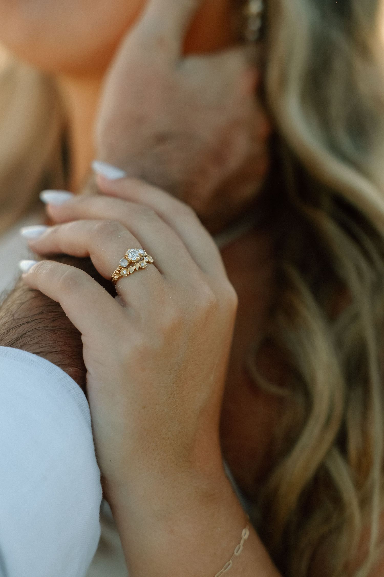 Close-up of elegant gold diamond engagement ring and wedding band on brides hand in her hair.