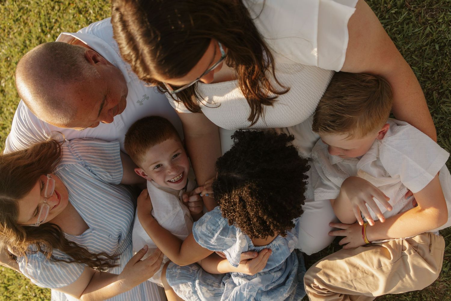 Aerial view of happy family hugging and laughing together on green grass.