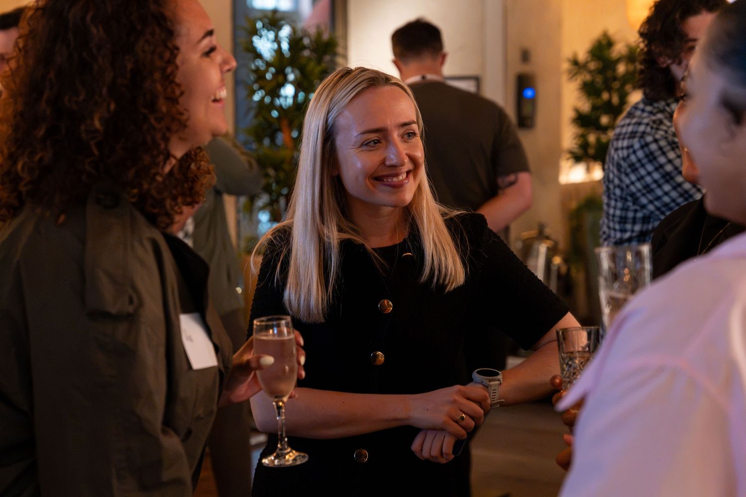 Smiling blonde woman holding champagne glass chatting at an evening social gathering.