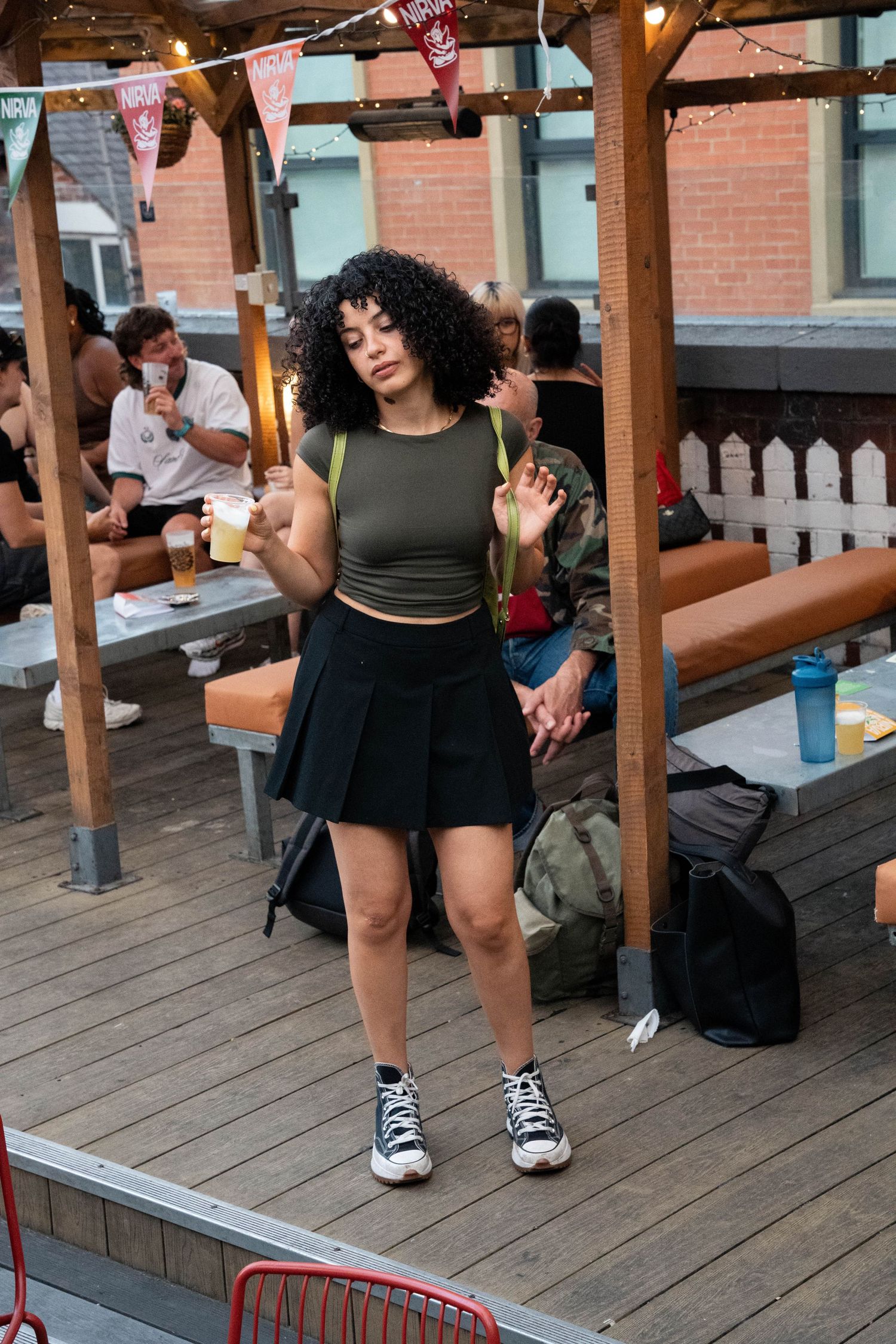 Young woman in green crop top and black skirt dancing on an outdoor patio.