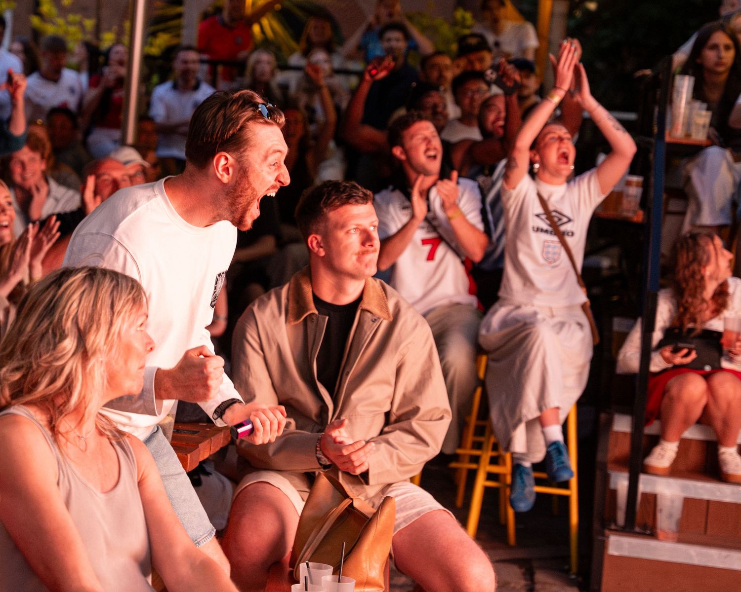 Enthusiastic fans reacting with joy while watching a sports match at an outdoor venue.