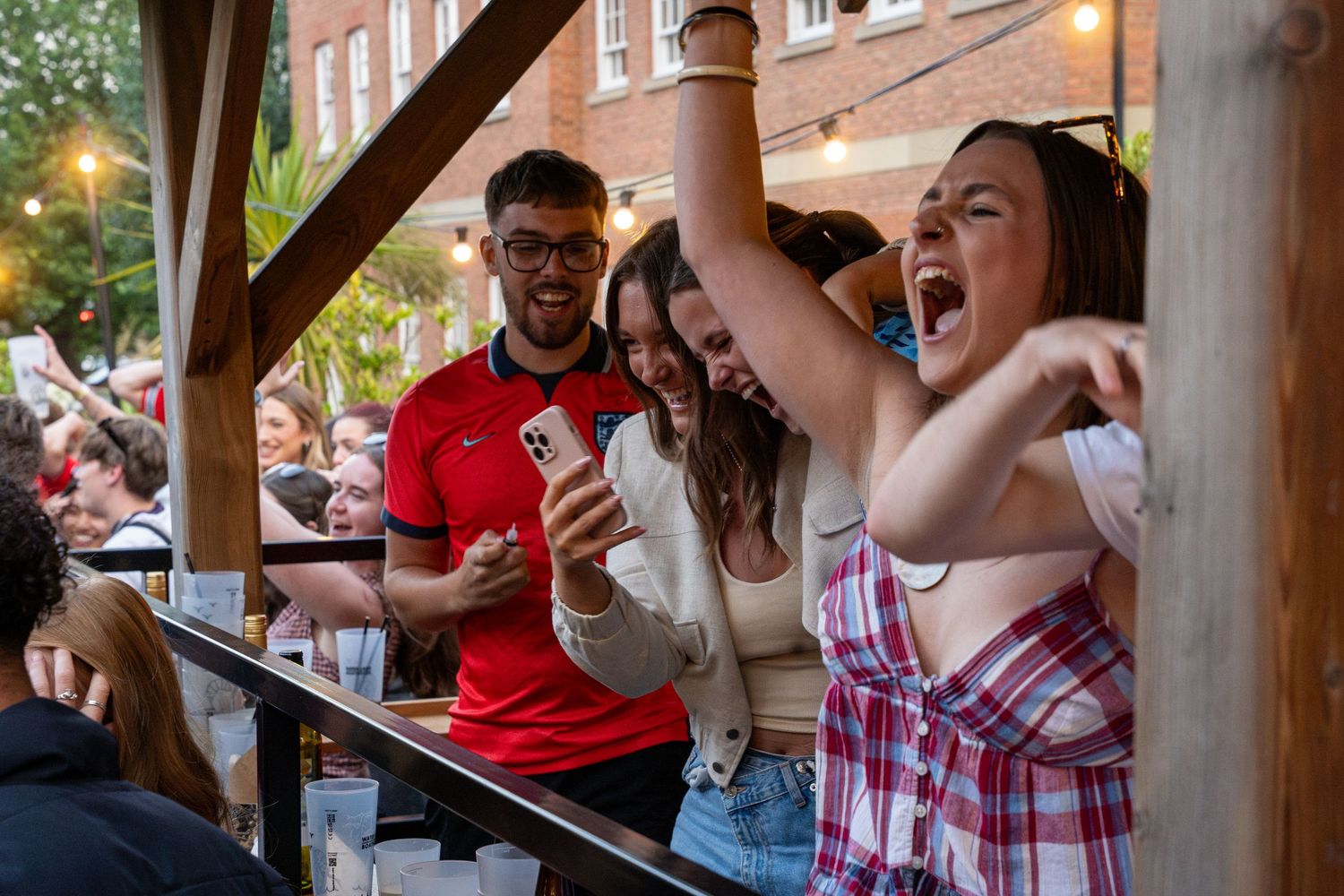 Excited group of friends cheering and laughing at an outdoor bar during a live sports event.