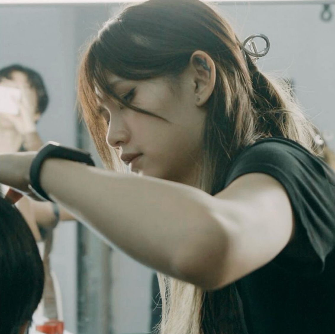 A young woman with long hair styling another person's hair in a professional salon setting.