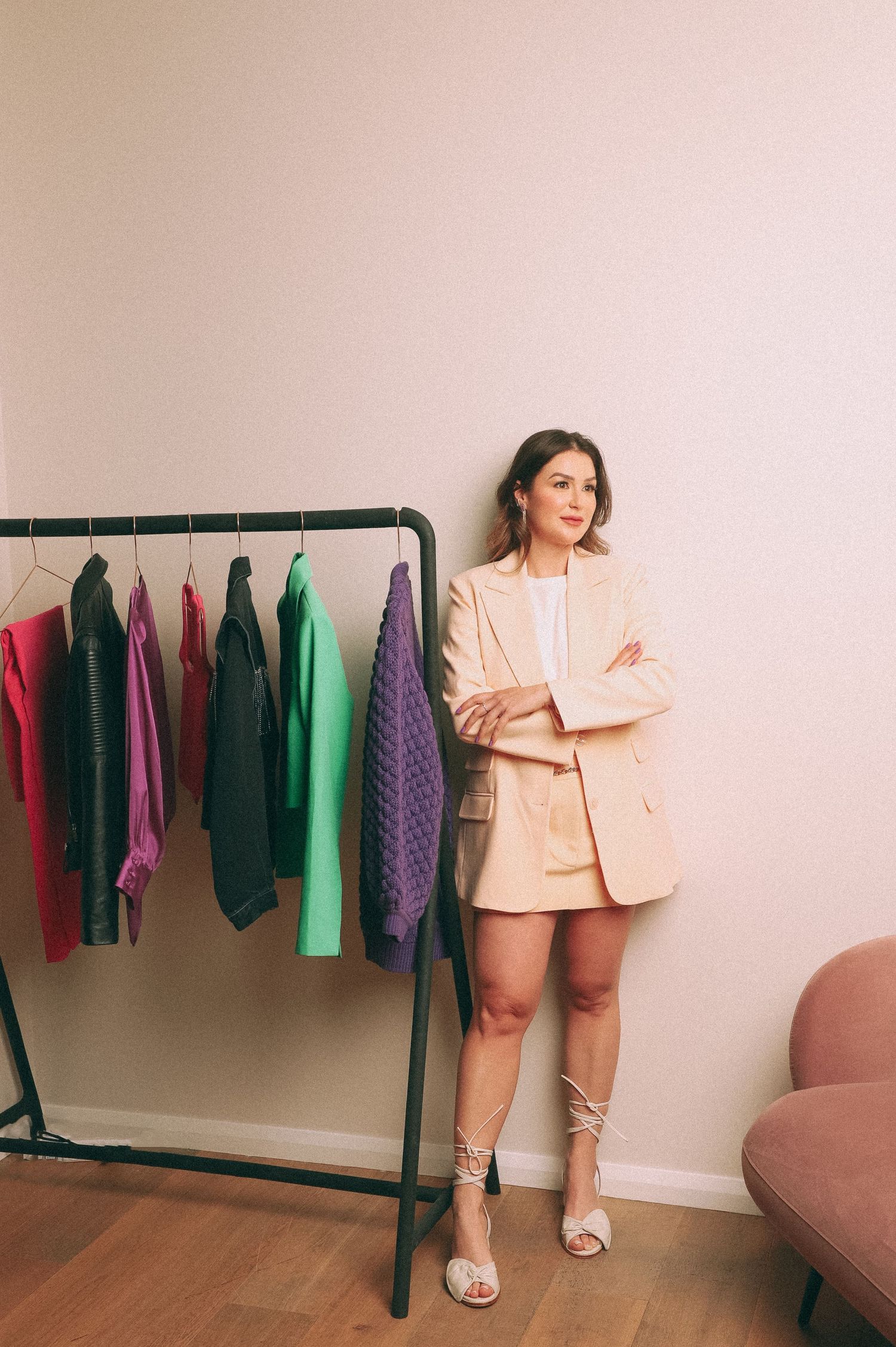 Branding Photography Sessions capture an entrepreneur in a beige blazer suit and strappy sandals standing next to a clothing rack.