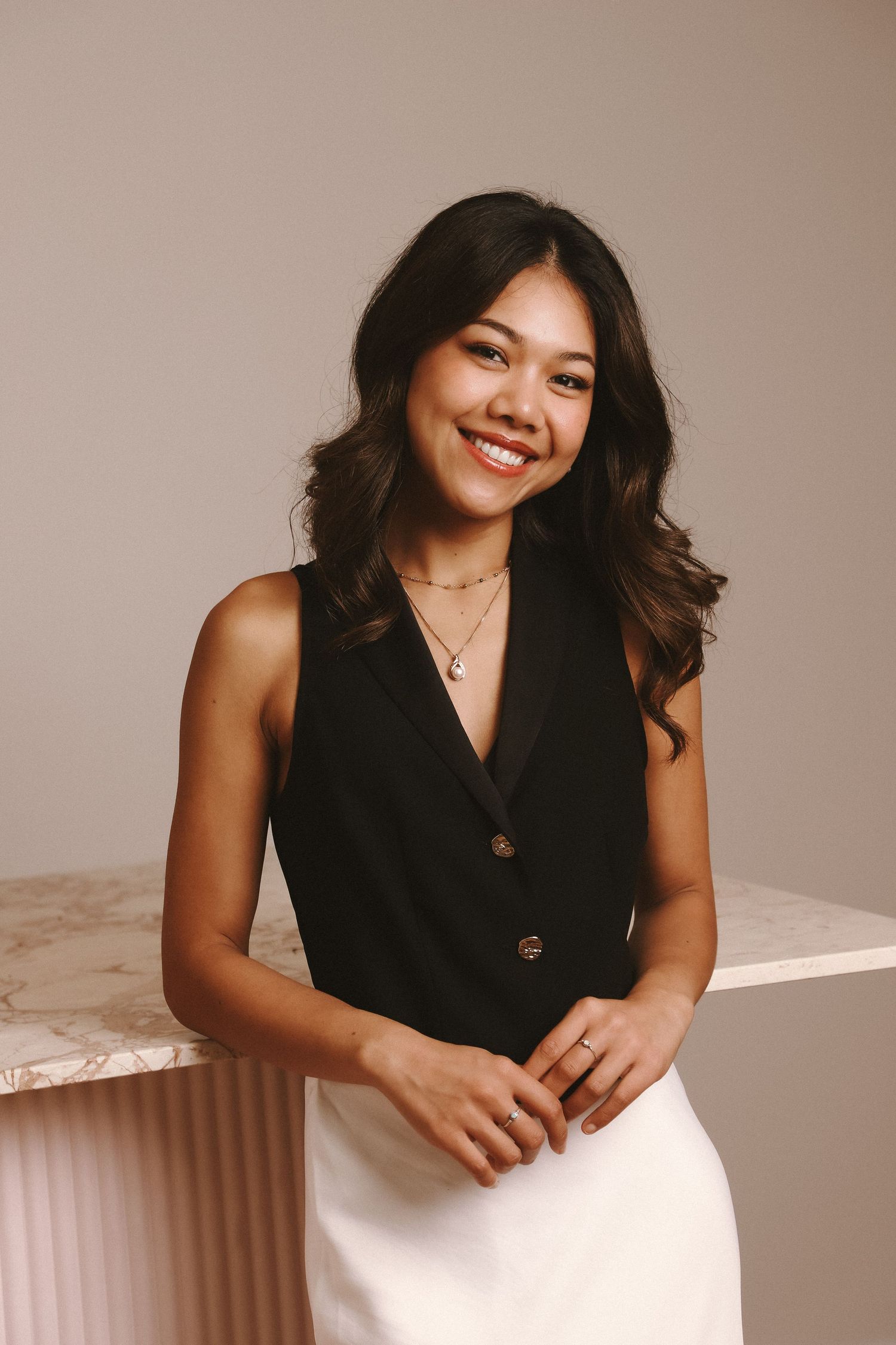 A joyful smile and dark wavy hair complement the black sleeveless top and white skirt in this warm-toned portrait.