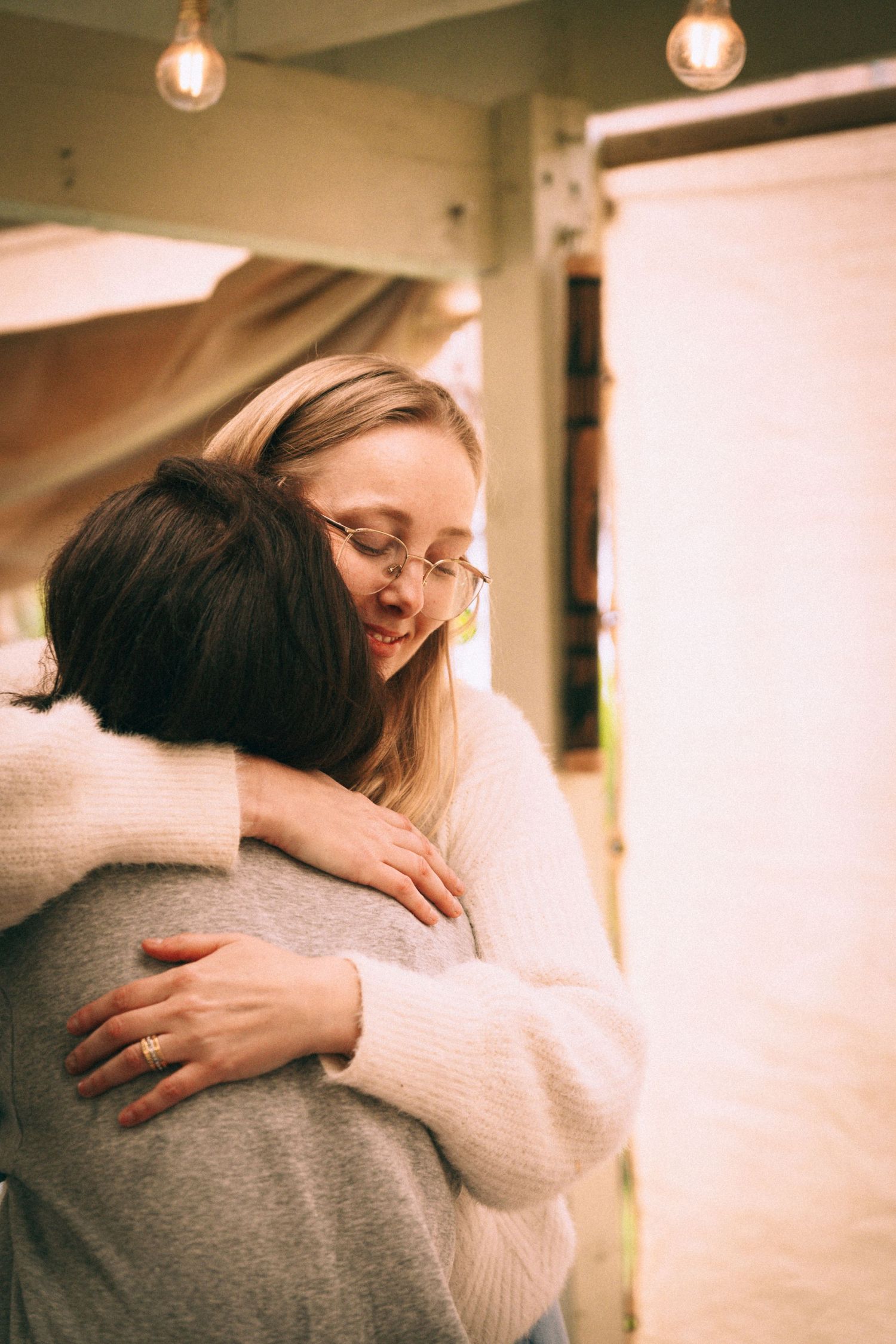 Branding Photography Sessions for a wellness coach capture two entrepreneurs sharing a warm embrace in cozy sweaters in a softly lit indoor