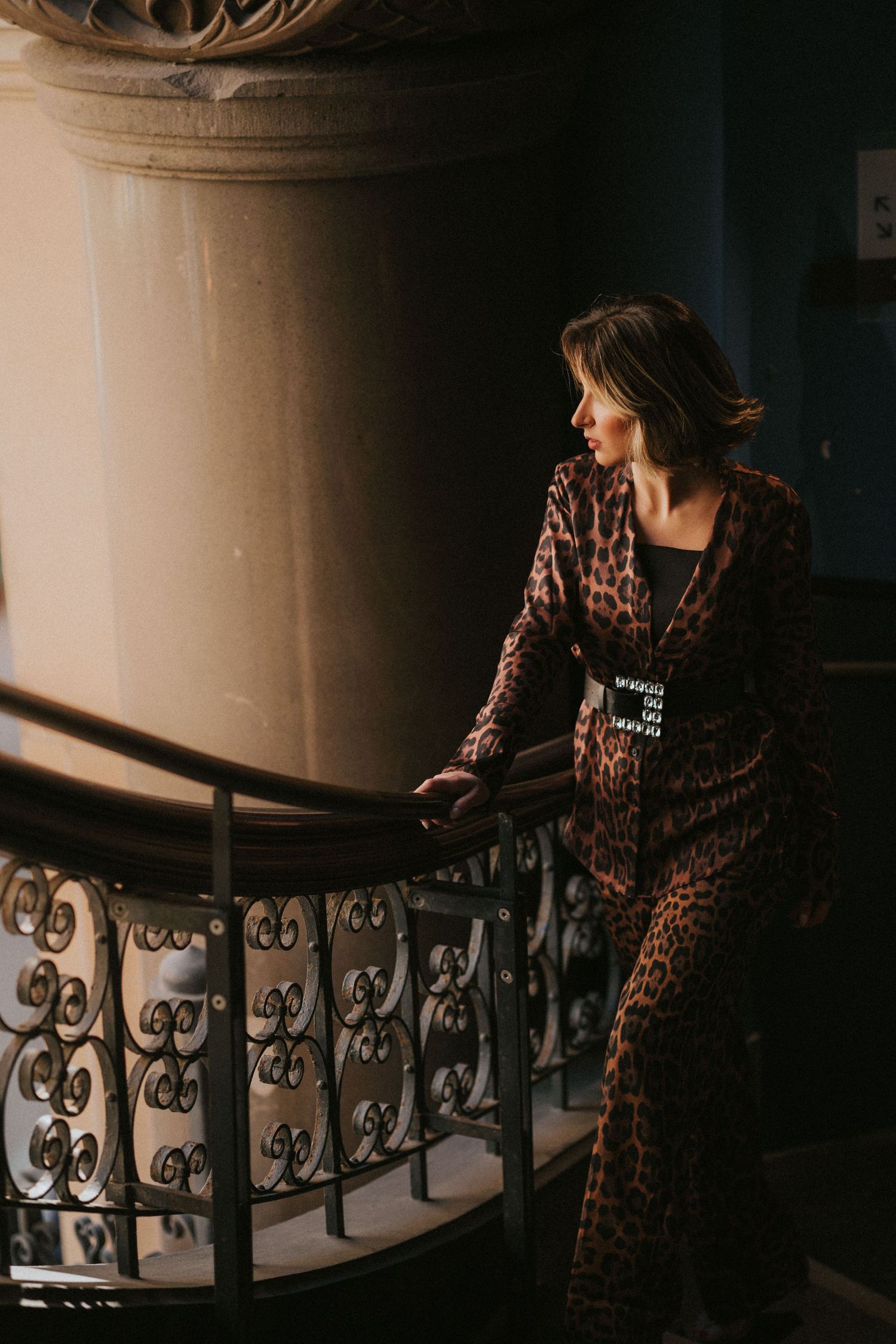 Branding Photography Sessions capture a stylist in a leopard print dress posing on an ornate spiral staircase with dramatic lighting.