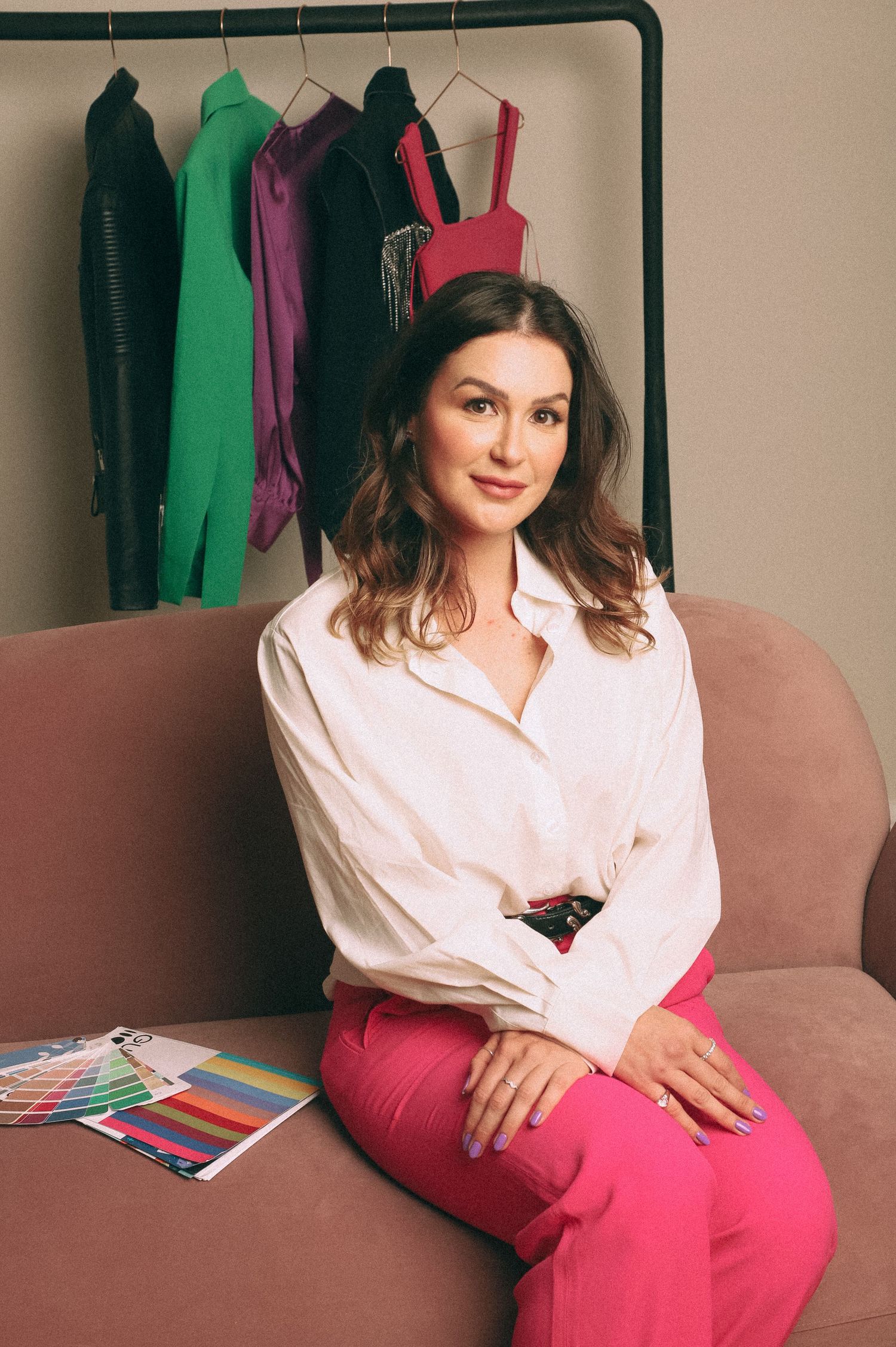 Branding Photography Sessions capture an entrepreneur in a light pink blouse and bright pink pants sitting on a brown couch.