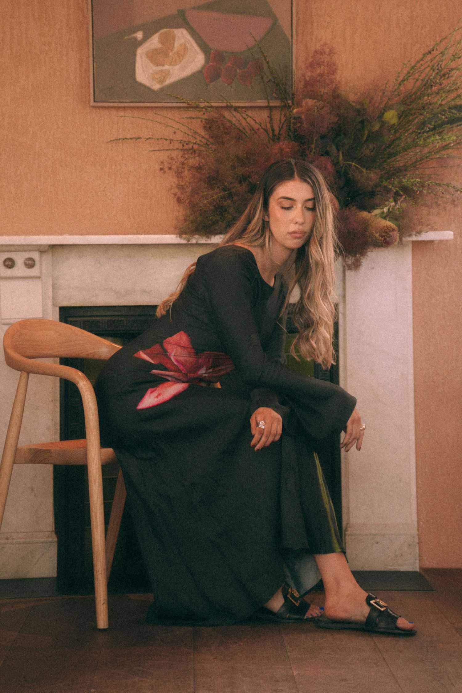 Branding Photography Sessions capture an entrepreneur in a black flowing dress sitting elegantly on a wooden chair in a warm-toned room