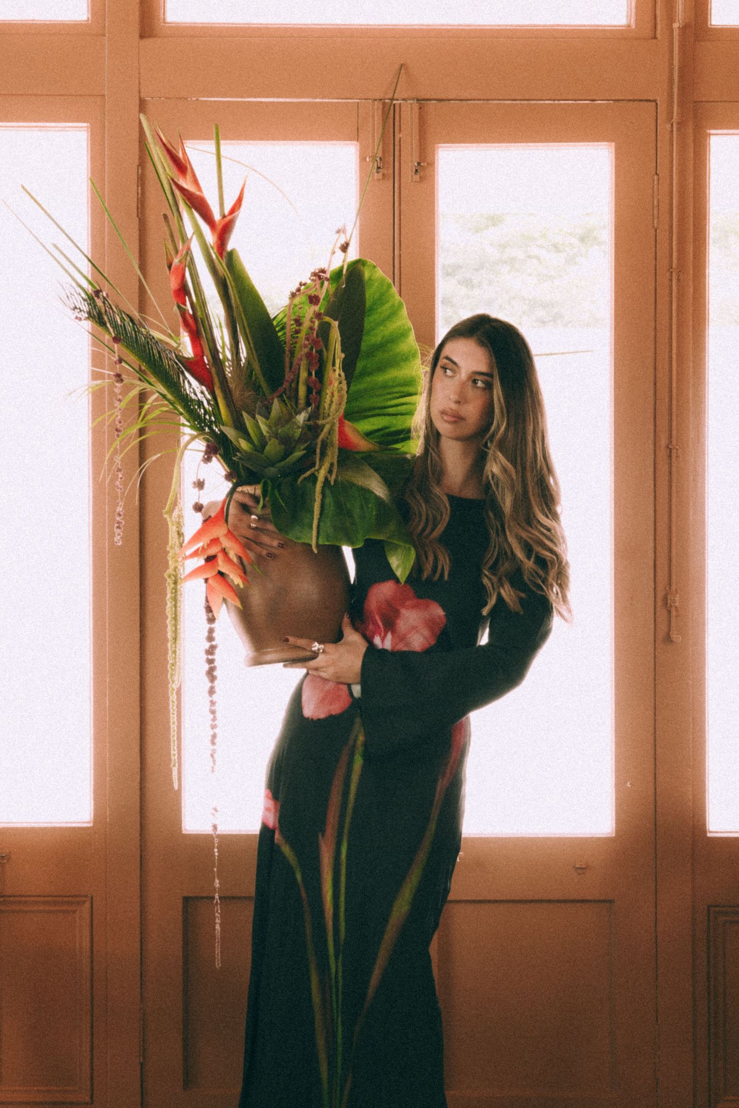 Branding Photography Sessions capture an entrepreneur in a black dress holding a dramatic tropical flower arrangement with birds of paradise
