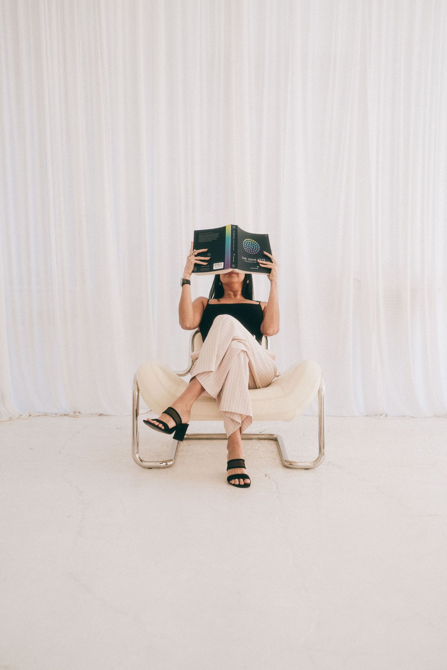 Branding Photography Sessions capture a coach in a beige outfit sitting on a chair, reading a book while covering their face.