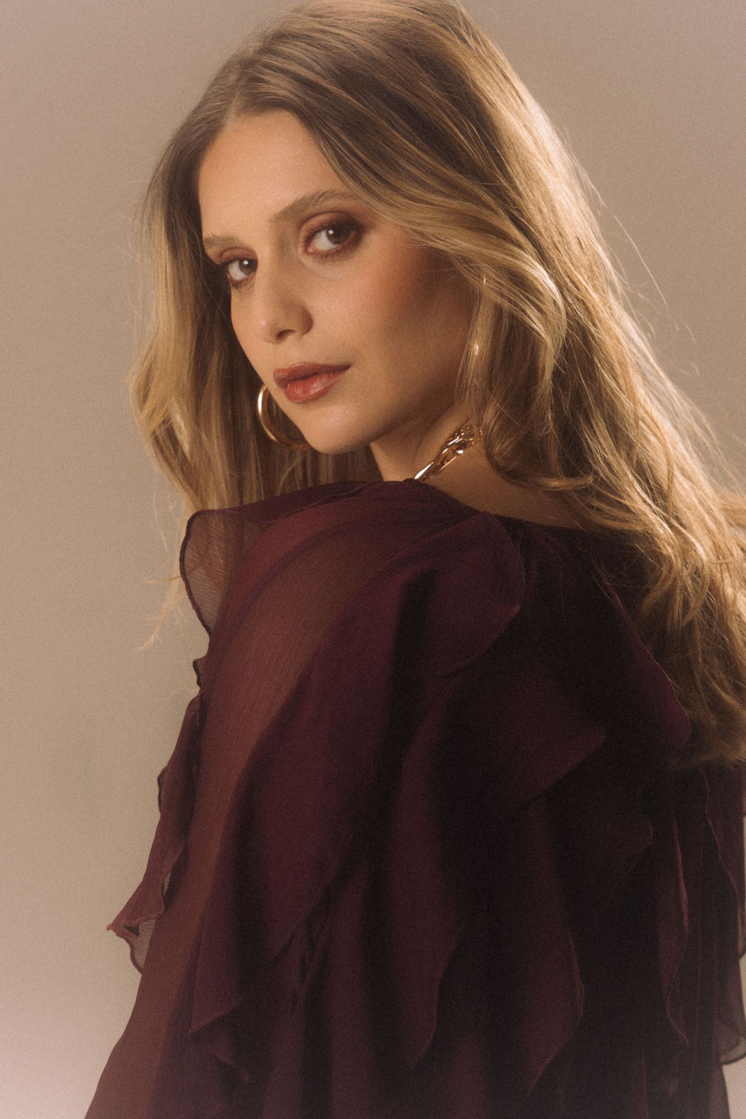 A fashion portrait showing a model in a burgundy ruffled collar blouse with soft lighting and wavy brown hair.