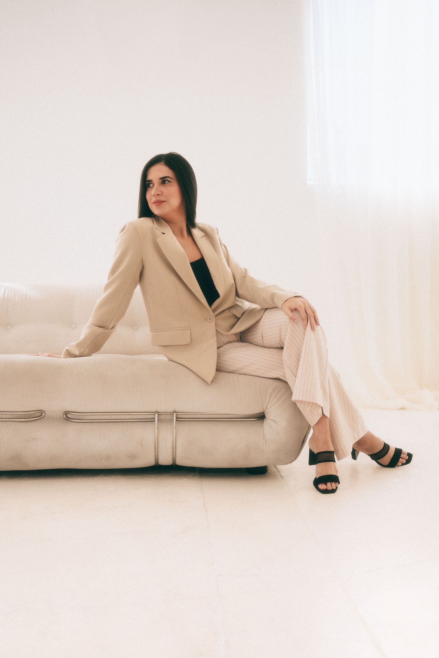 Branding Photography Sessions capture an entrepreneur in a beige business suit and black sandals posing elegantly on a light-colored sofa