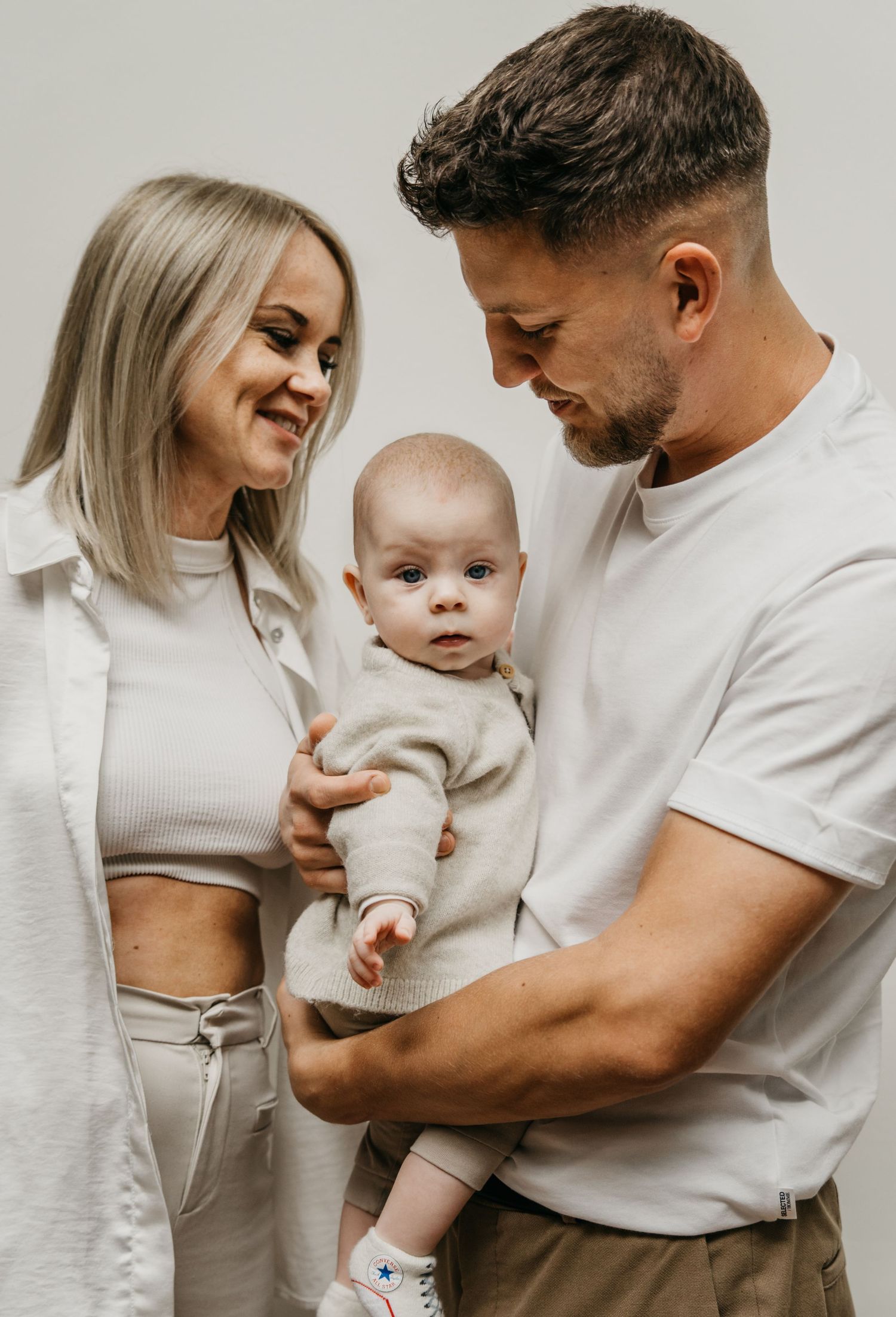 Smiling mother and father hold their curious baby in a bright studio family portrait.