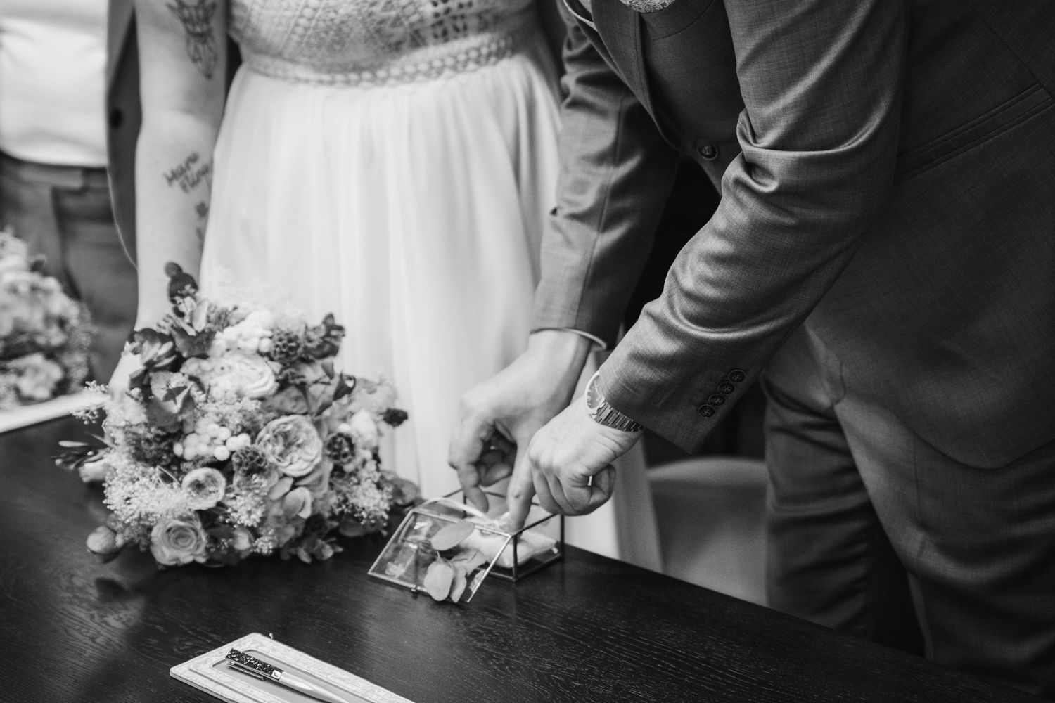 Black and white photo of a bride and groom signing their marriage certificate beside a bouquet of roses.