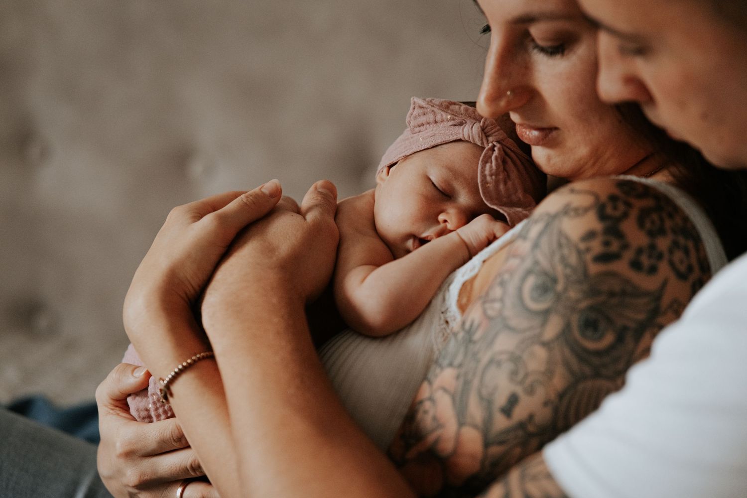 Paar kuschelt liebevoll mit seinem schlafenden Neugeborenen mit rosa Haarband für ein inniges Familienporträt.