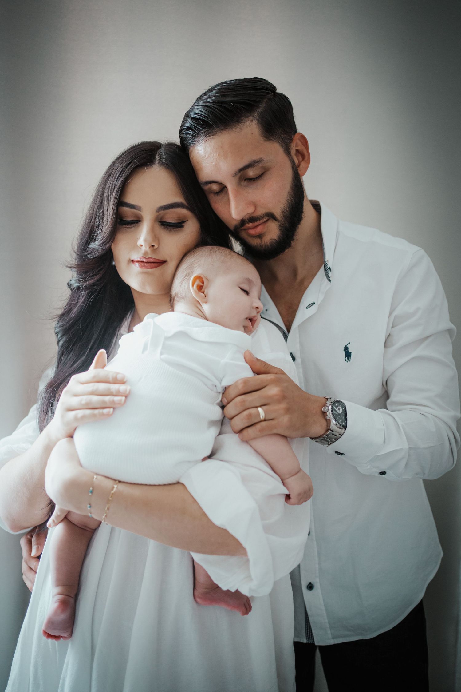Mutter und Vater in weißen Outfits halten ihr schlafendes Neugeborenes liebevoll in den Armen für ein ruhiges Familienporträt.