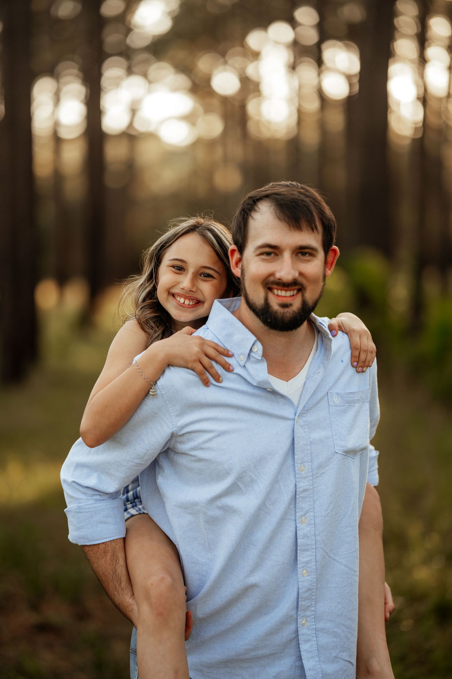 Two figures share a piggyback pose while smiling in a forest with golden sunset lighting.