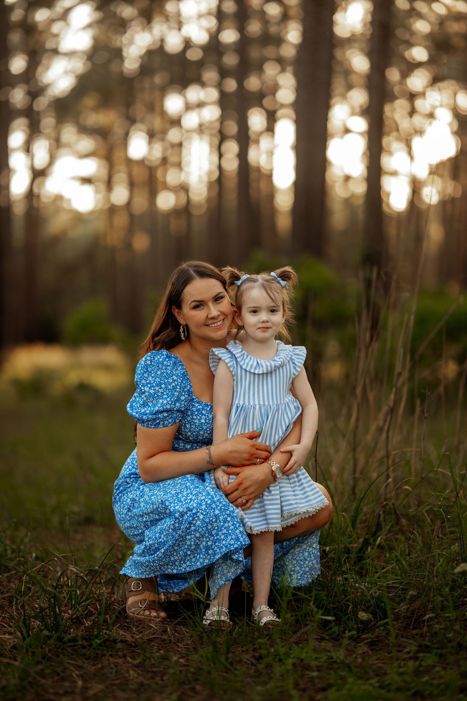 A touching portrait showing tender moment between two people in blue dresses against forest backdrop at dusk.