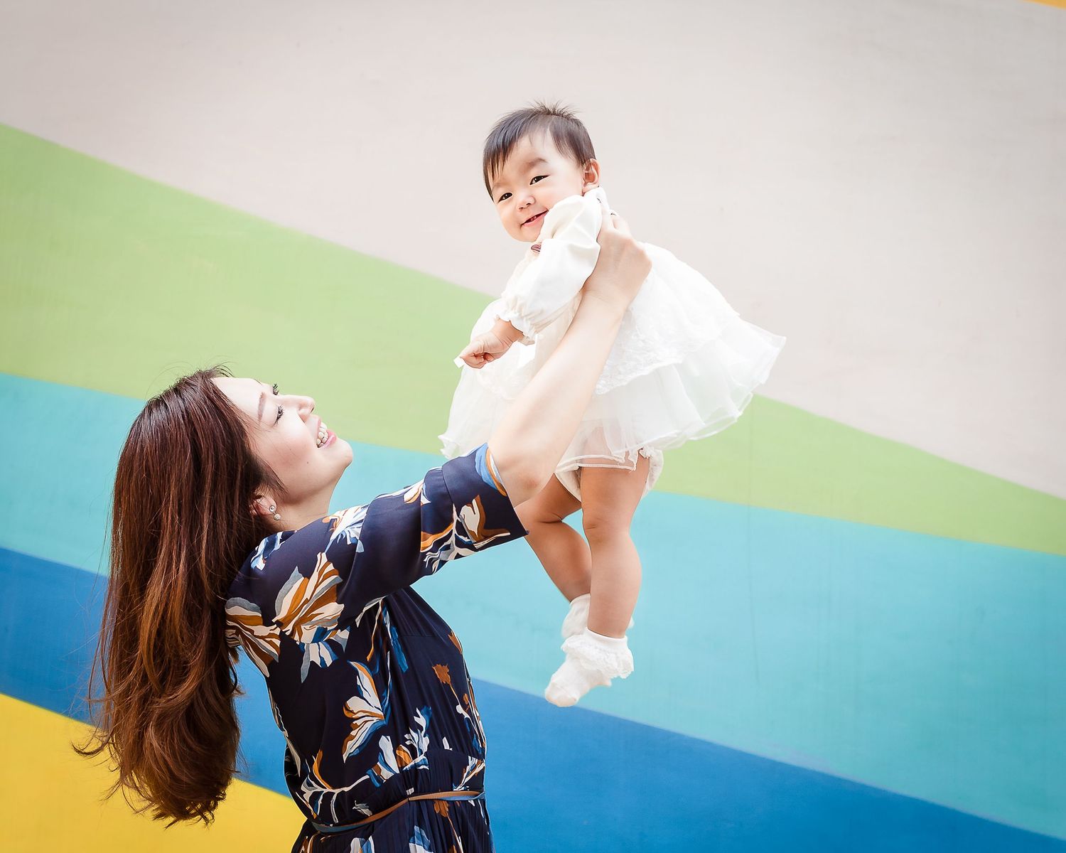 A joyful parent-child play moment against a colorful striped wall background.