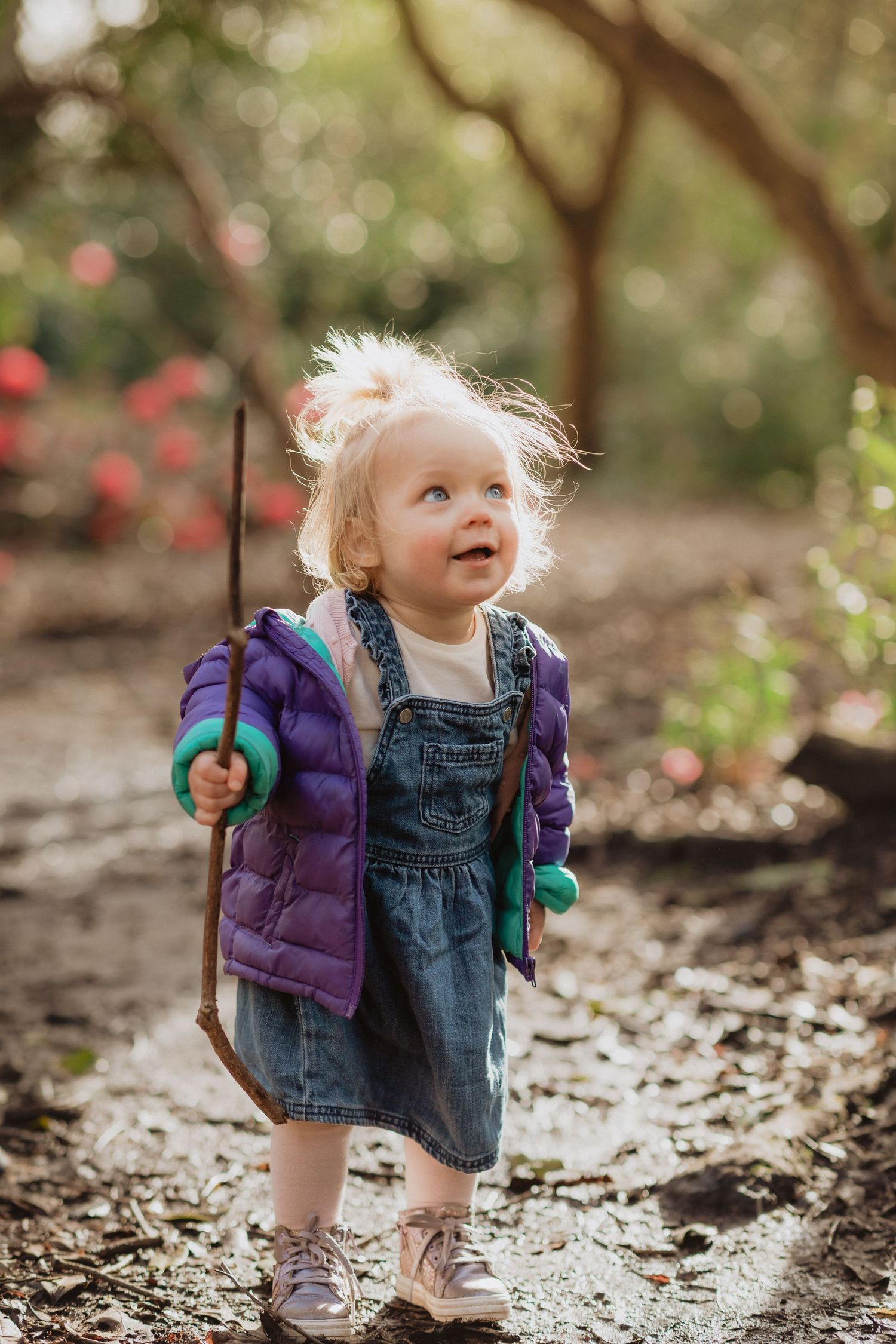 Small child in purple puffer jacket and denim dress exploring outdoors on fallen leaves.