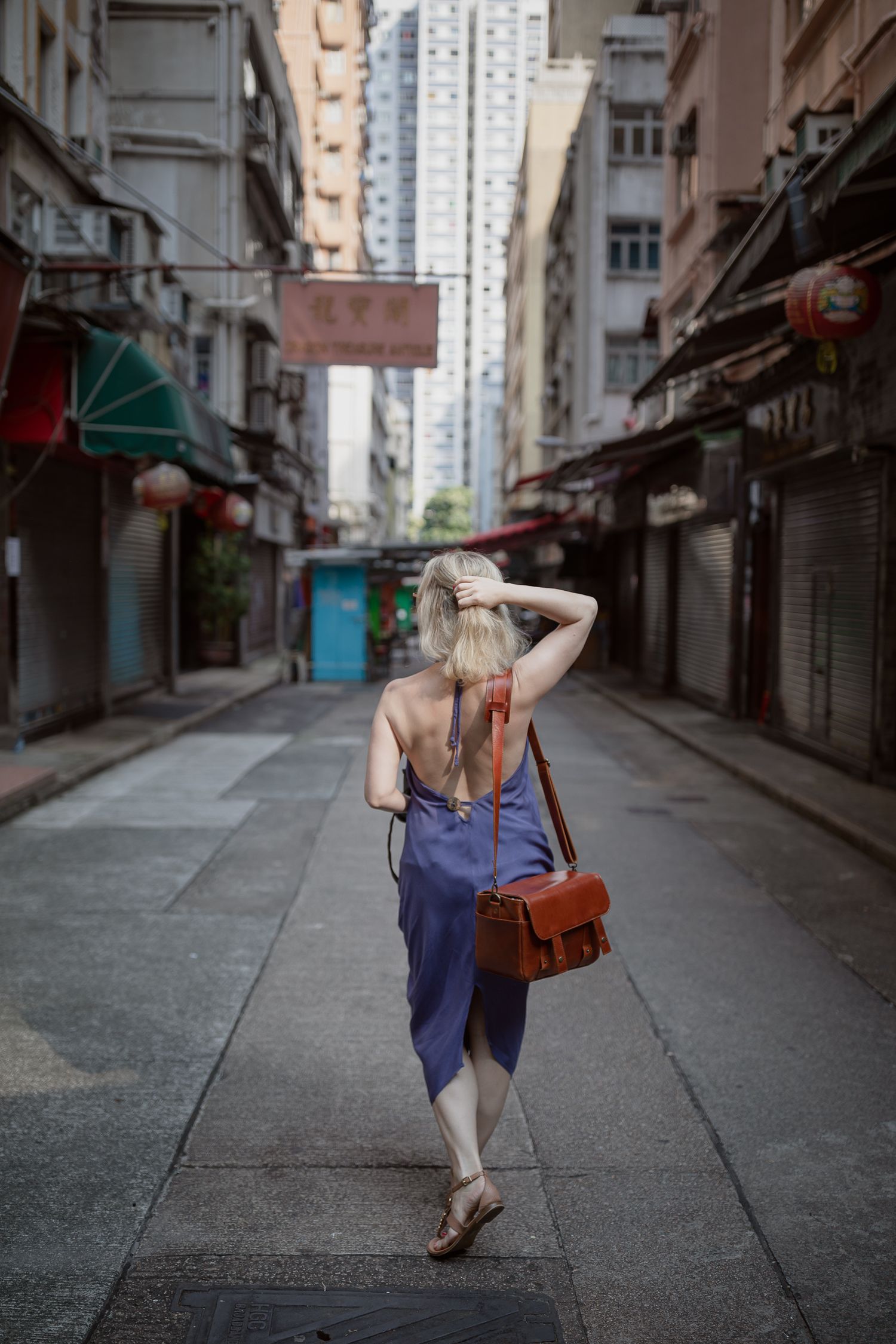 Person walking down empty urban alley with tall buildings and market stalls.