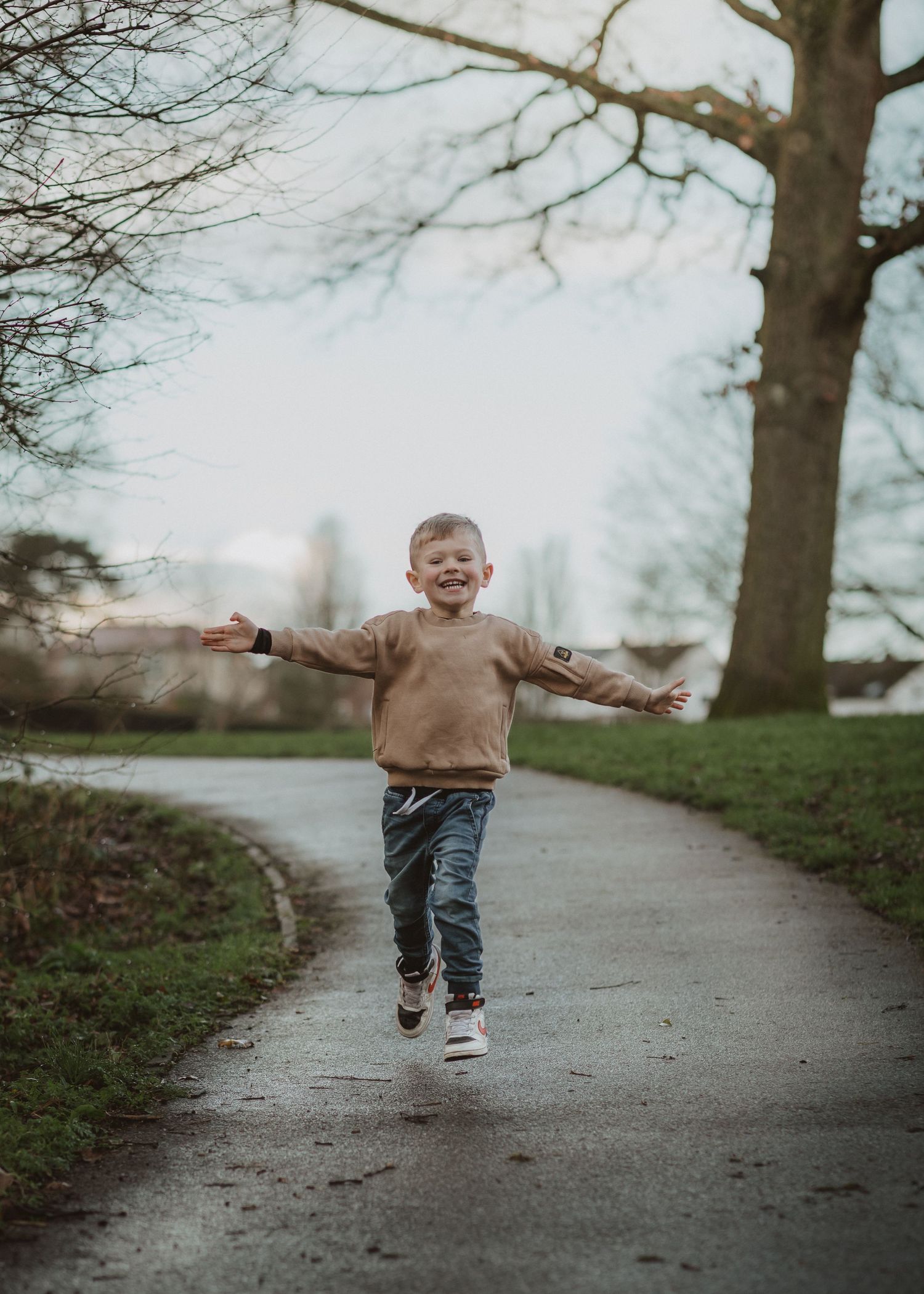 Young child running joyfully on a path beneath bare winter trees.