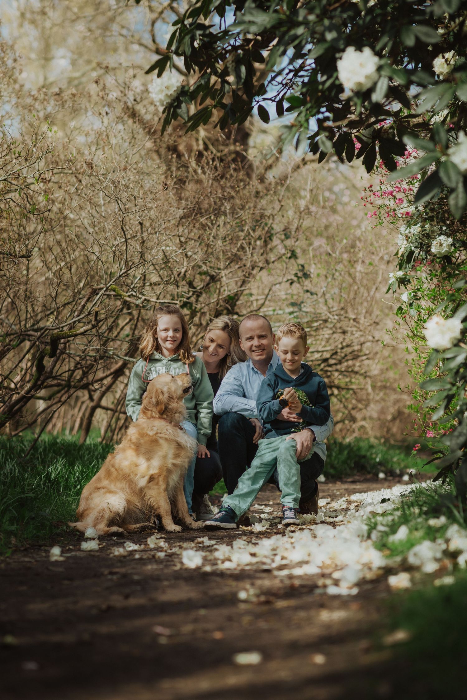 Family relaxing together outdoors with their dog among blooming flowers.